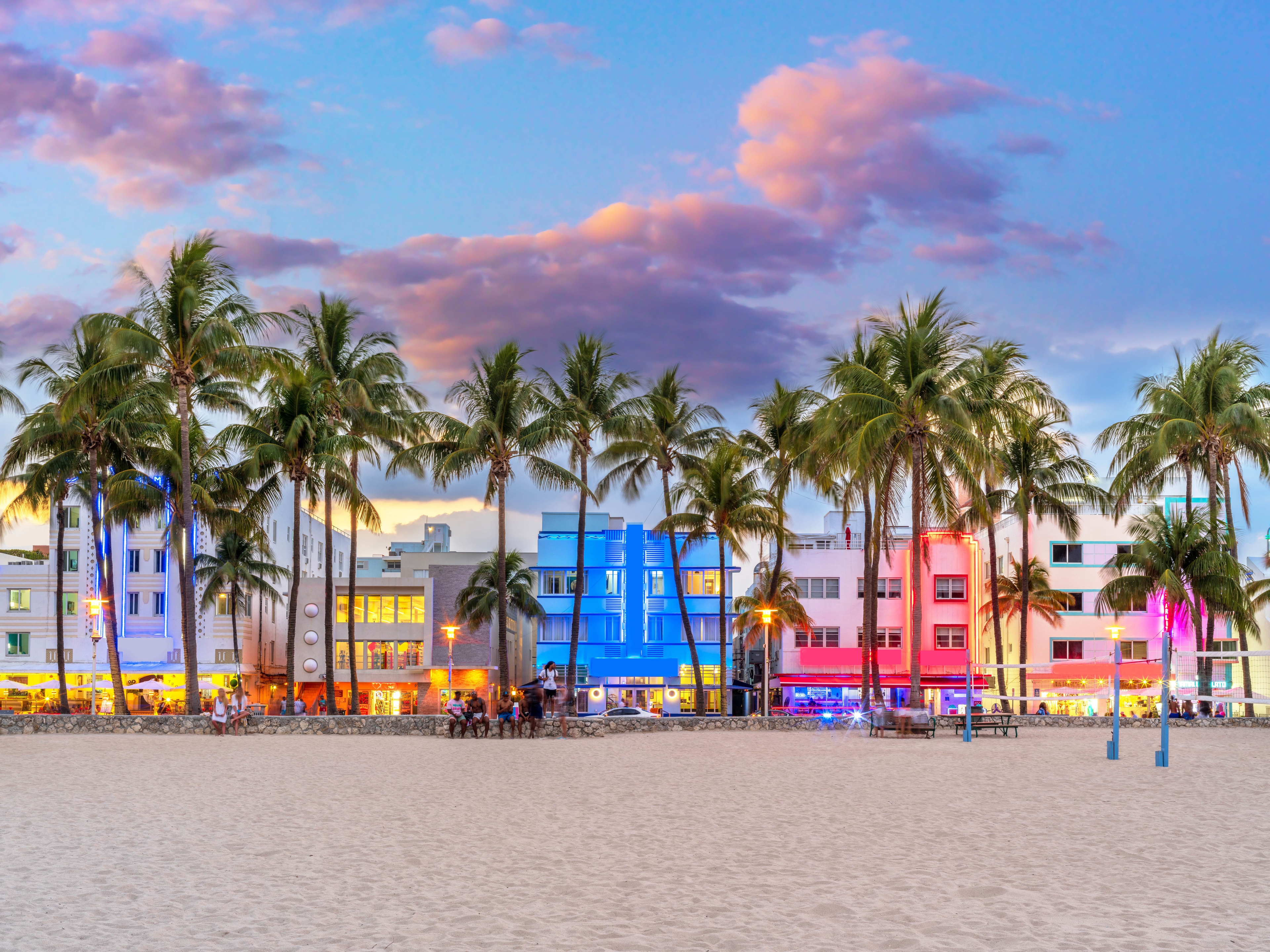 Colorful art deco buildings and swaying palm trees along Miami's iconic Ocean Drive at sunset, viewed from the sandy beach.