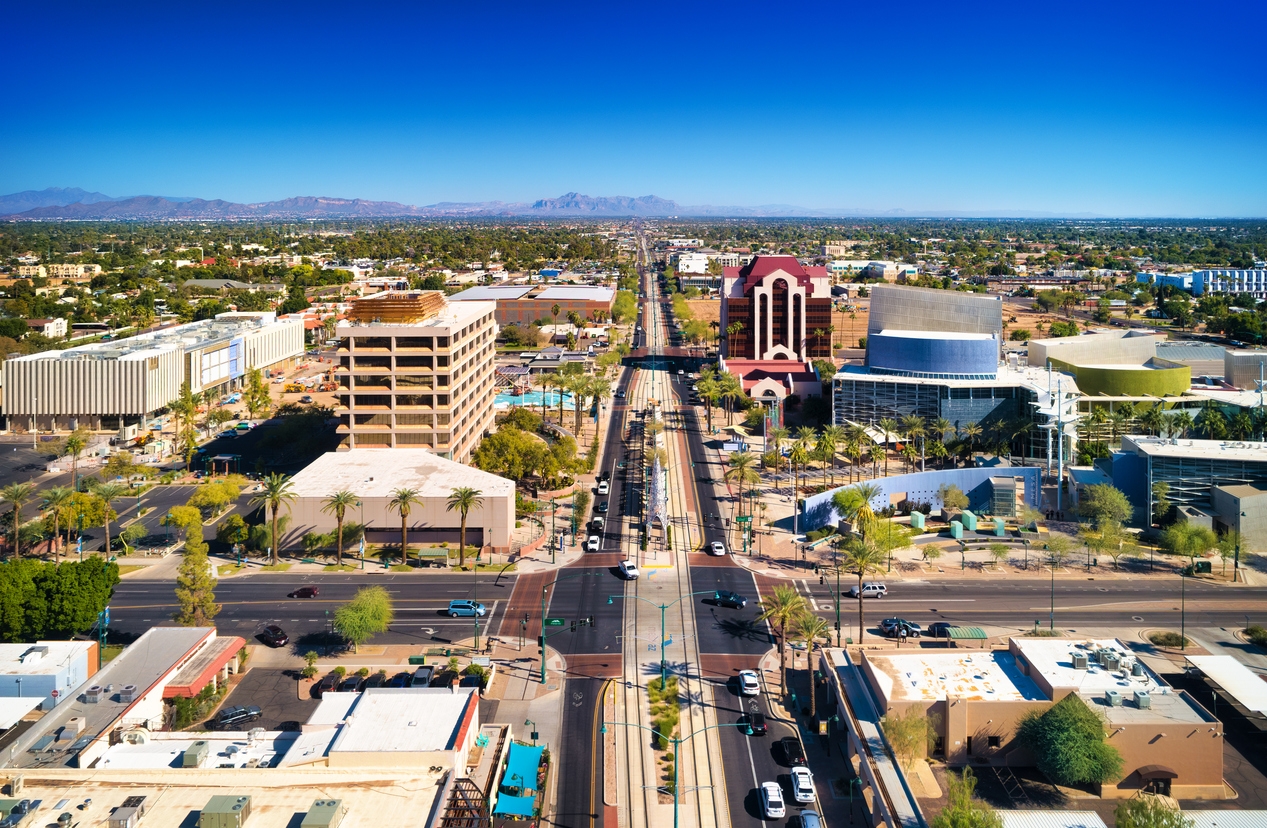 Aerial view of downtown Mesa, Arizona featuring modern architecture, wide streets, and desert landscapes with the Superstition Mountains in the distance.