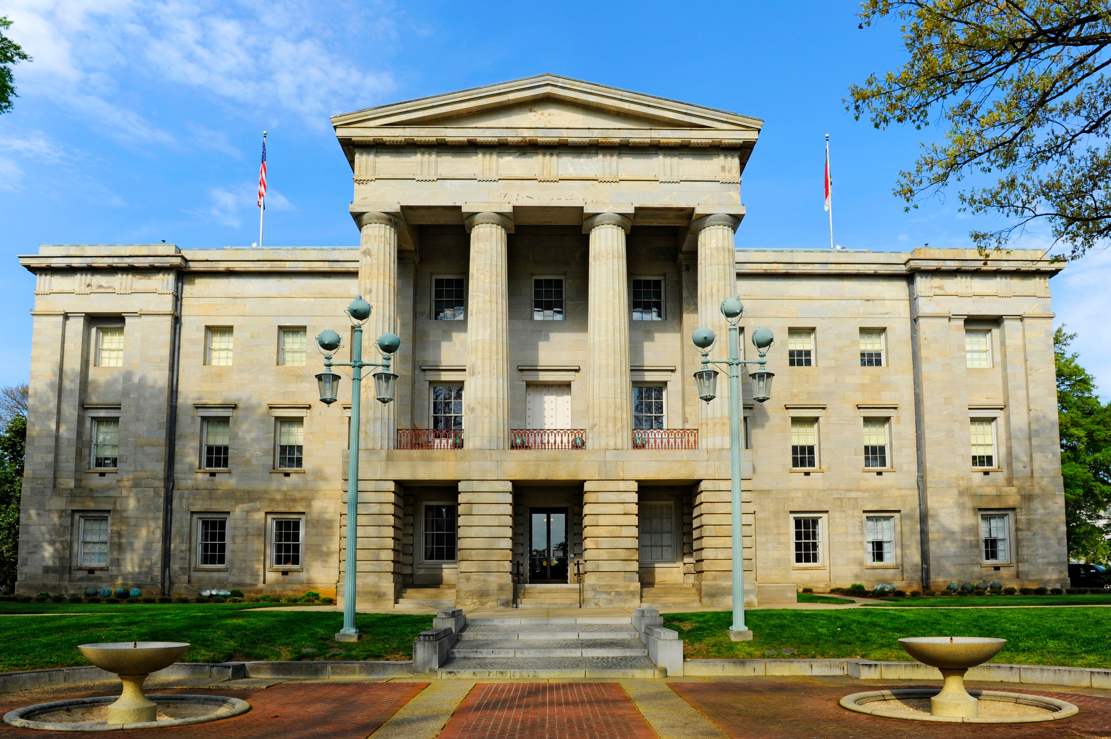 Front view of the North Carolina State Capitol in Raleigh, featuring neoclassical architecture with tall columns and symmetrical design under a clear blue sky.