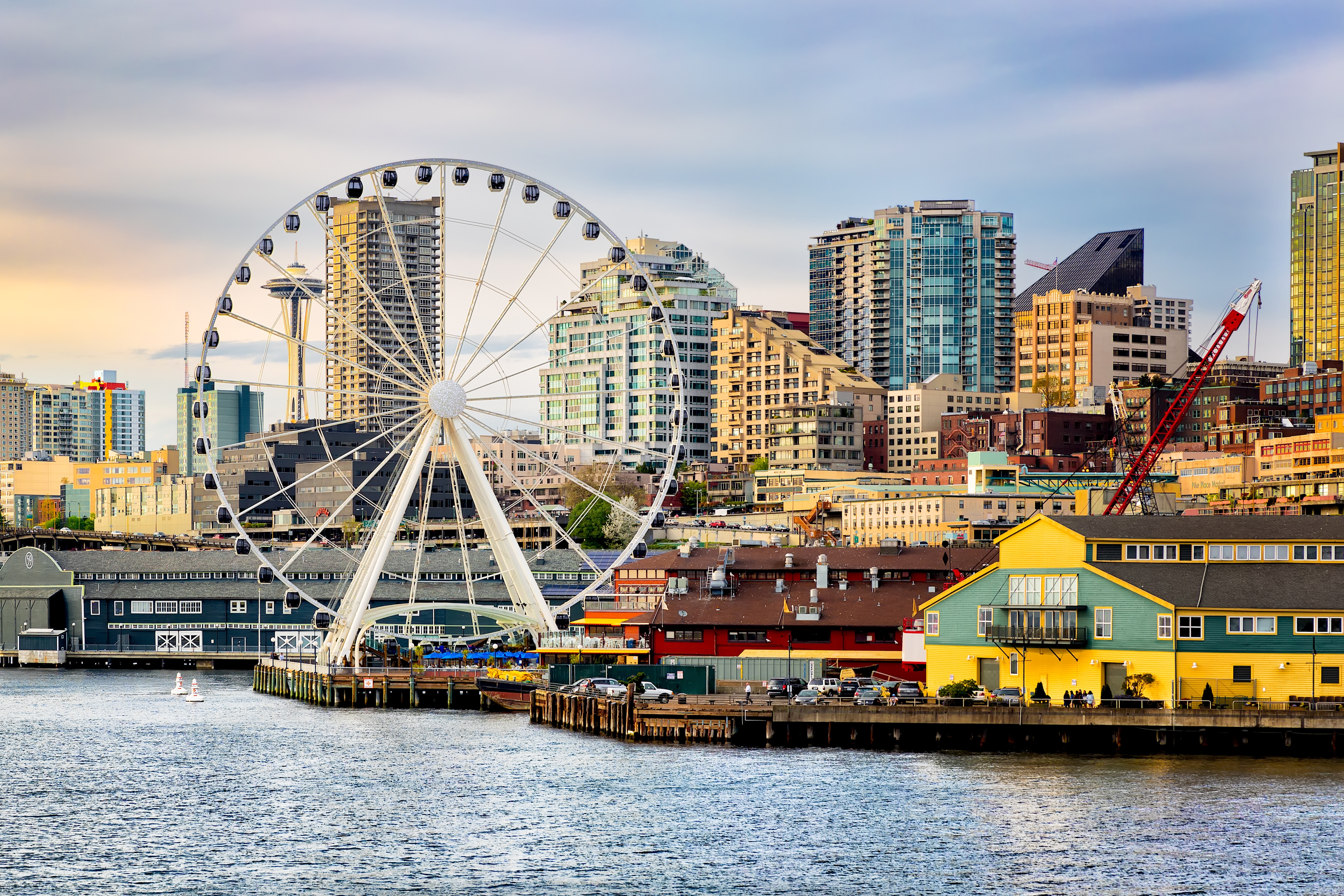 Scenic view of Seattle’s waterfront featuring the Seattle Great Wheel, colorful pier buildings, and downtown high-rises at sunset.