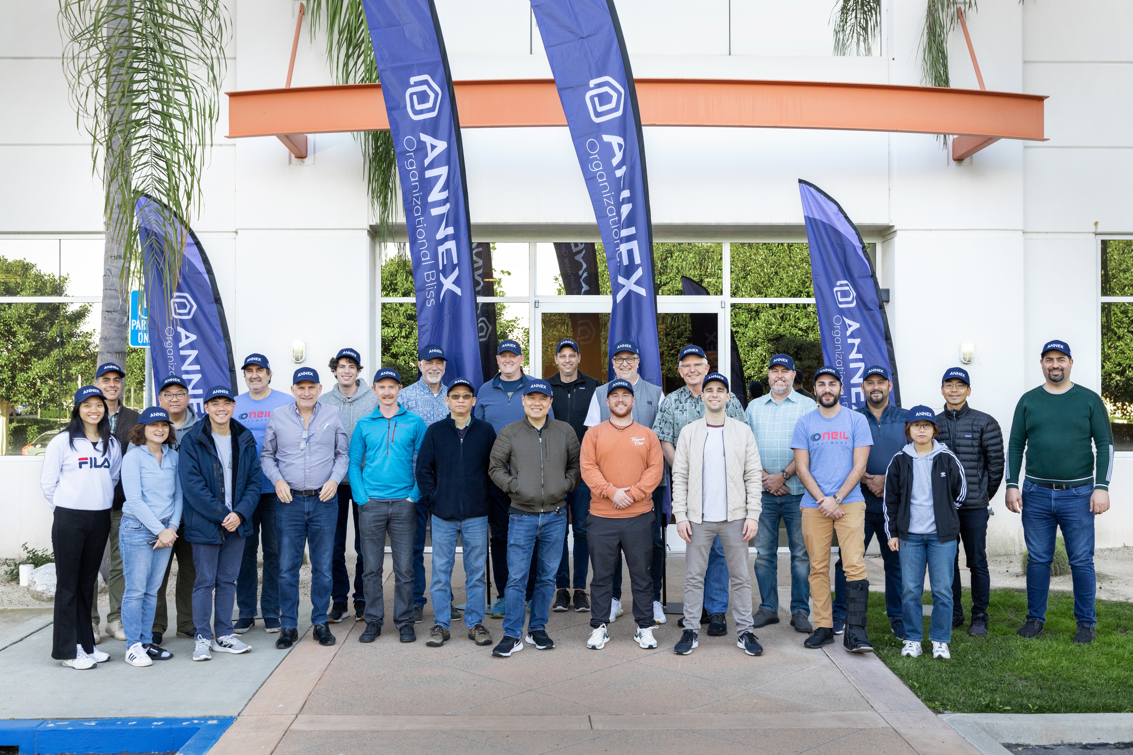 A group of coworkers wearing hats that say Annex, standing in front of large purple flags.