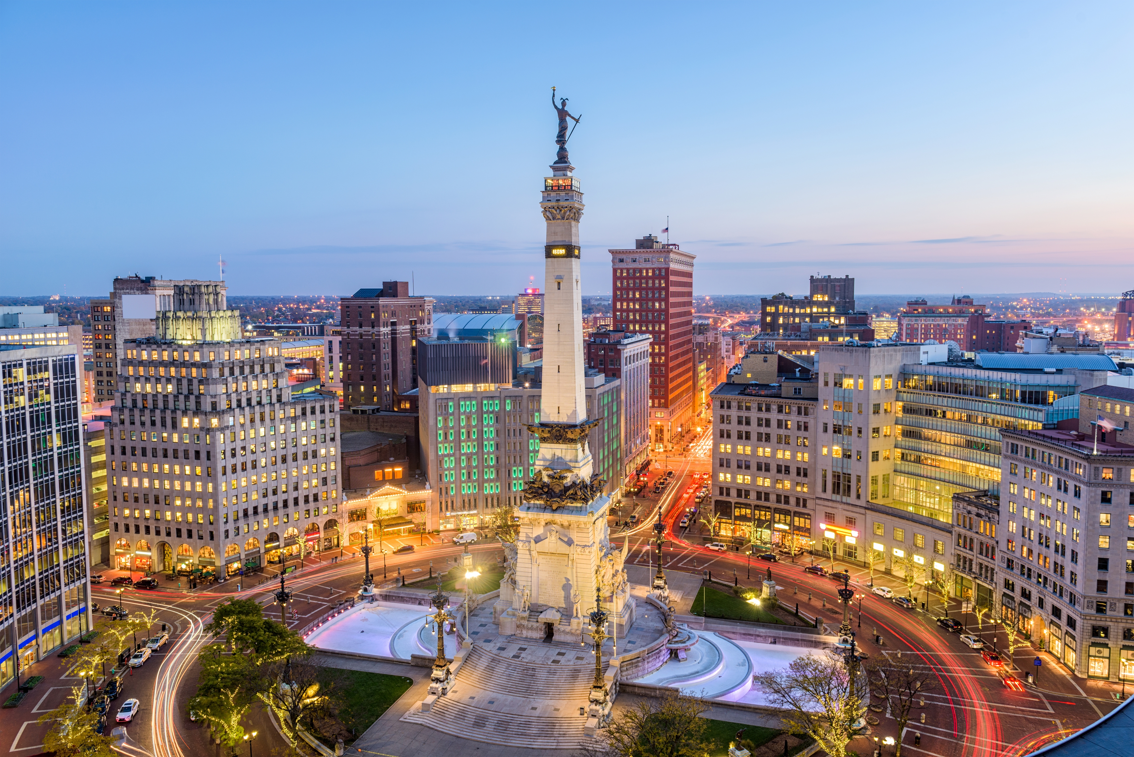 Downtown Indianapolis at twilight featuring the Soldiers and Sailors Monument surrounded by historic buildings and glowing city lights.