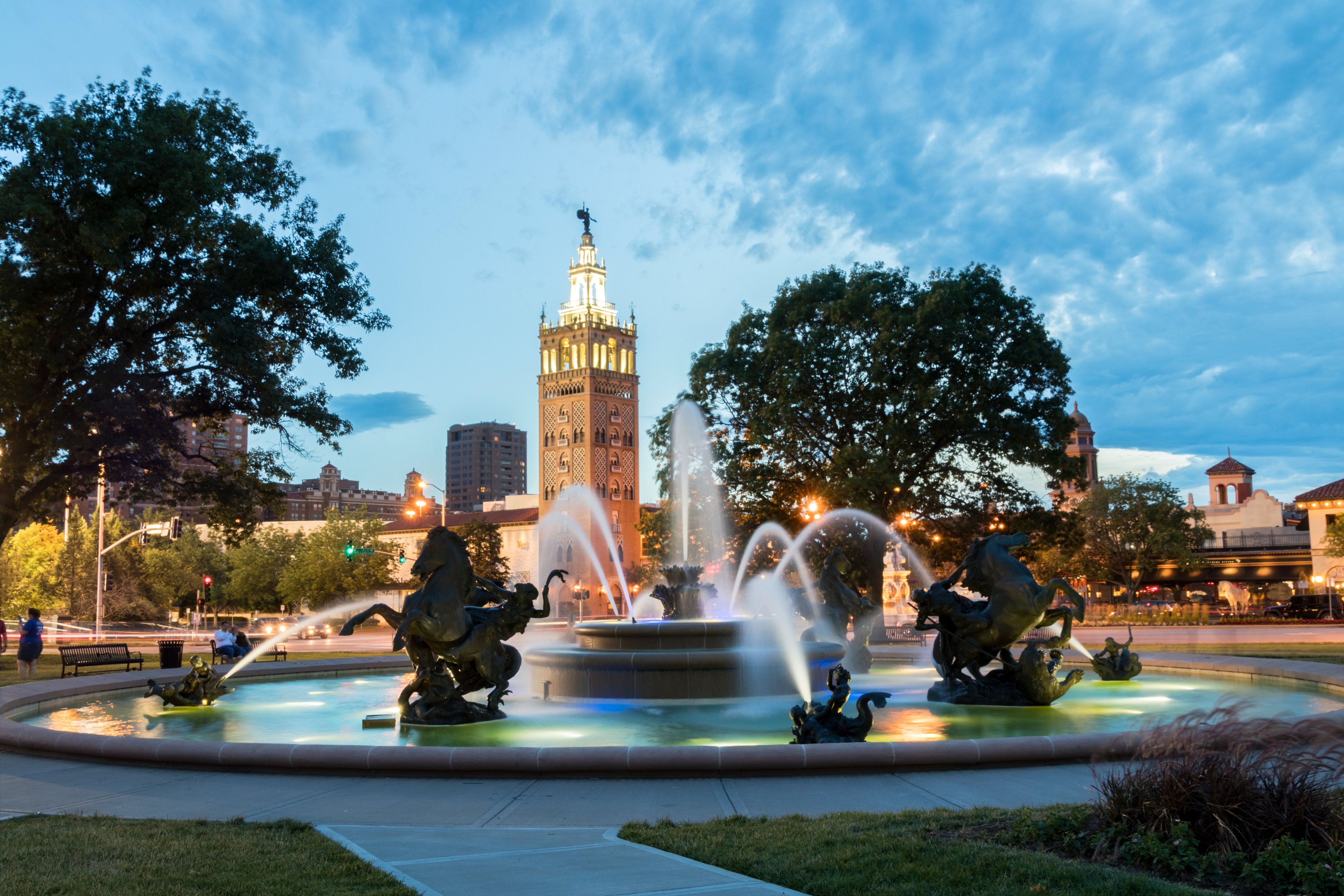 Kansas City’s J.C. Nichols Memorial Fountain at dusk with illuminated water jets, bronze horse sculptures, and the iconic Country Club Plaza tower in the background.
