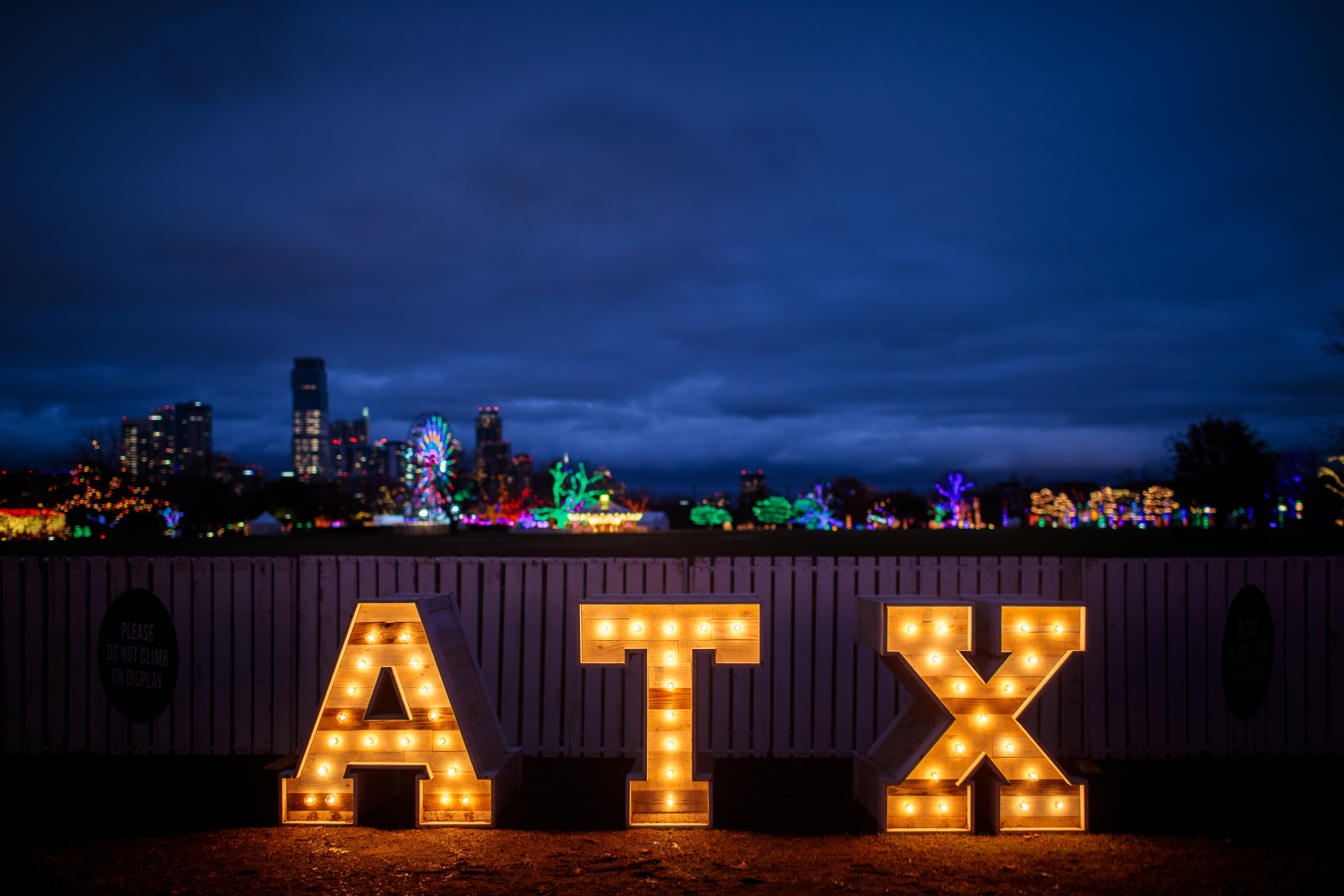 Festive illuminated "ATX" sign glowing at night in front of a vibrant Austin skyline and colorful holiday lights, capturing the spirit of the Texas capital.