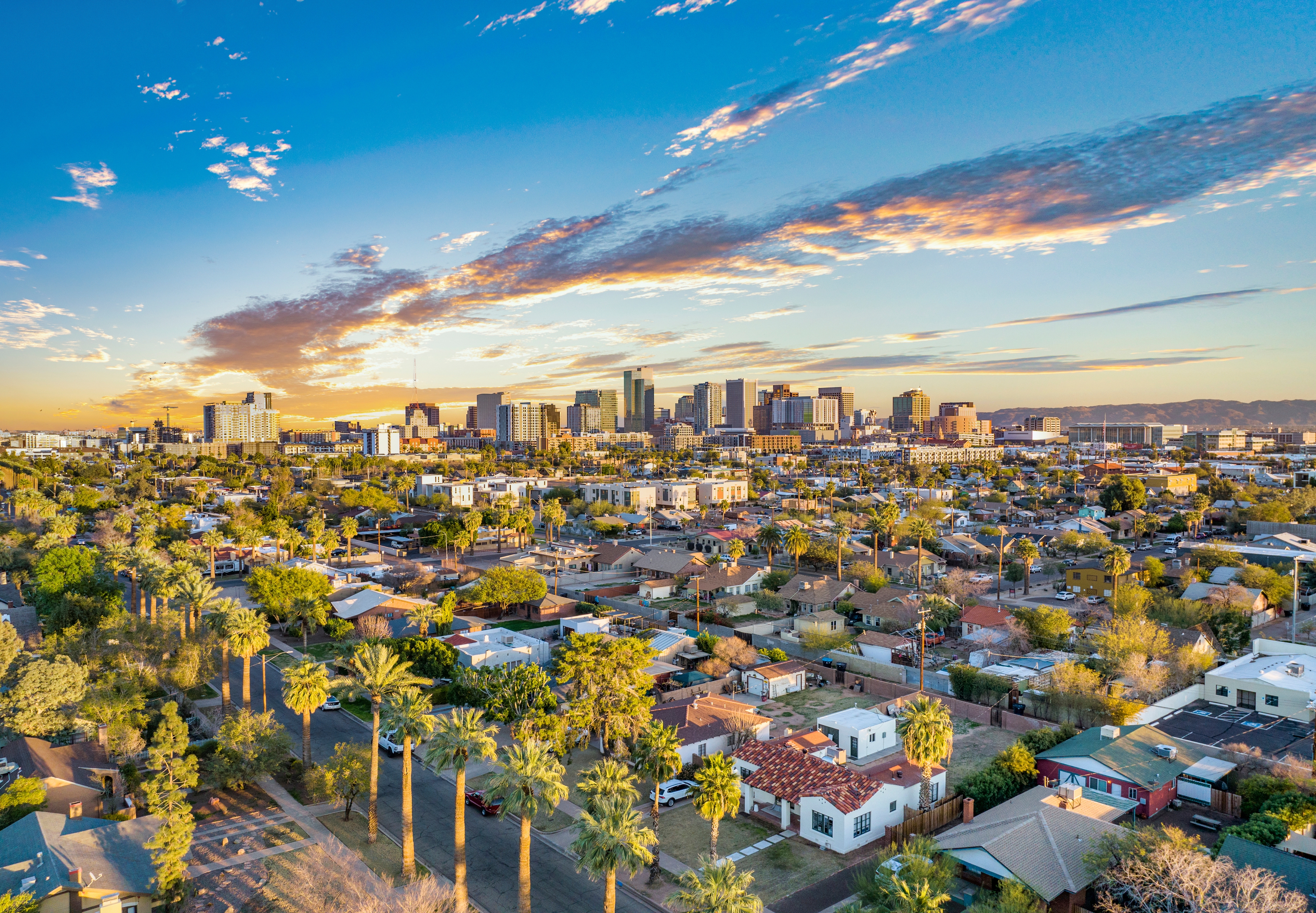 Aerial view of downtown Phoenix, Arizona with residential neighborhoods in the foreground and a vibrant sunset sky overhead.