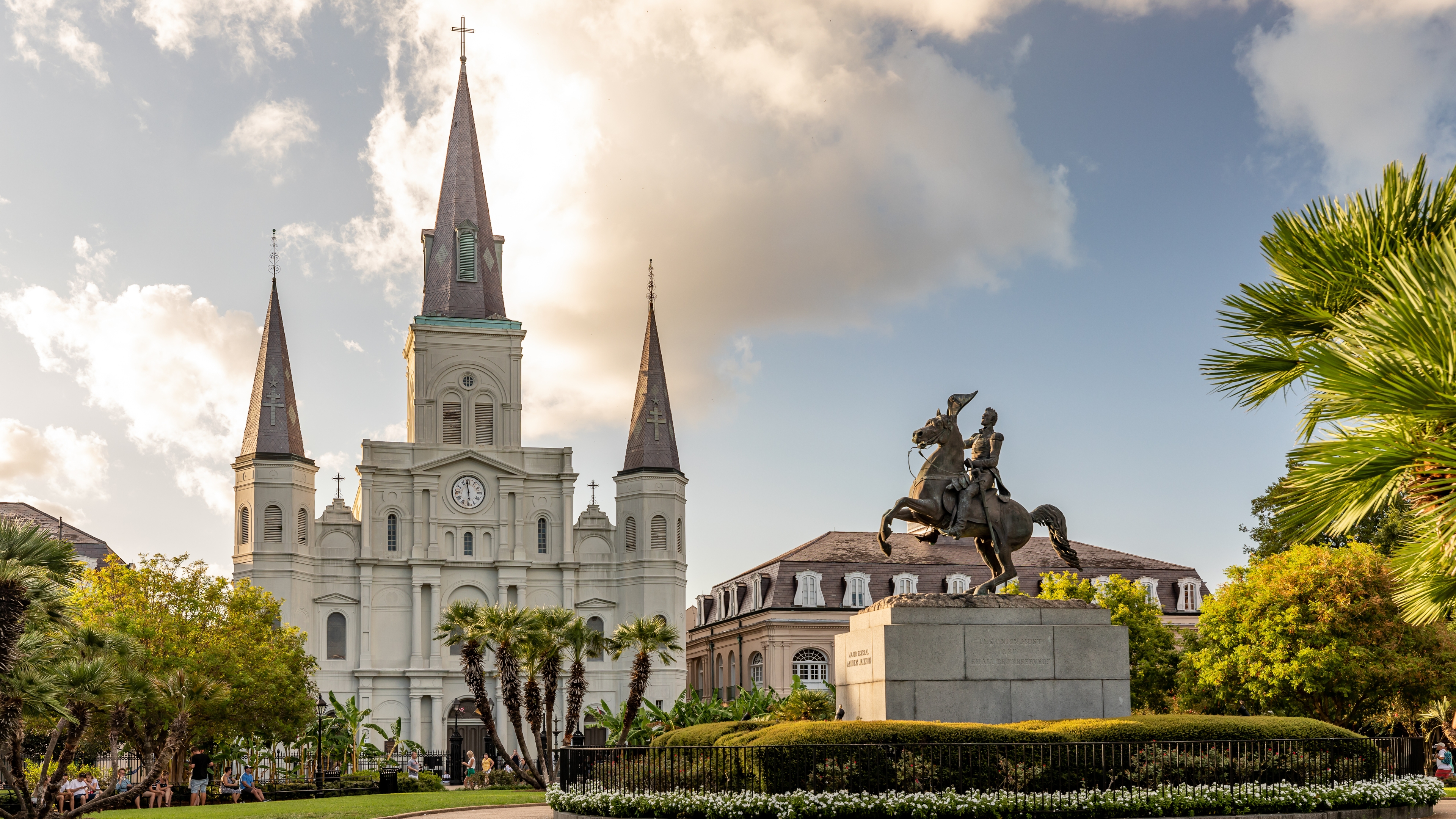 Classic view of St. Louis Cathedral and the Andrew Jackson statue in Jackson Square, New Orleans, framed by palm trees and a glowing afternoon sky.
