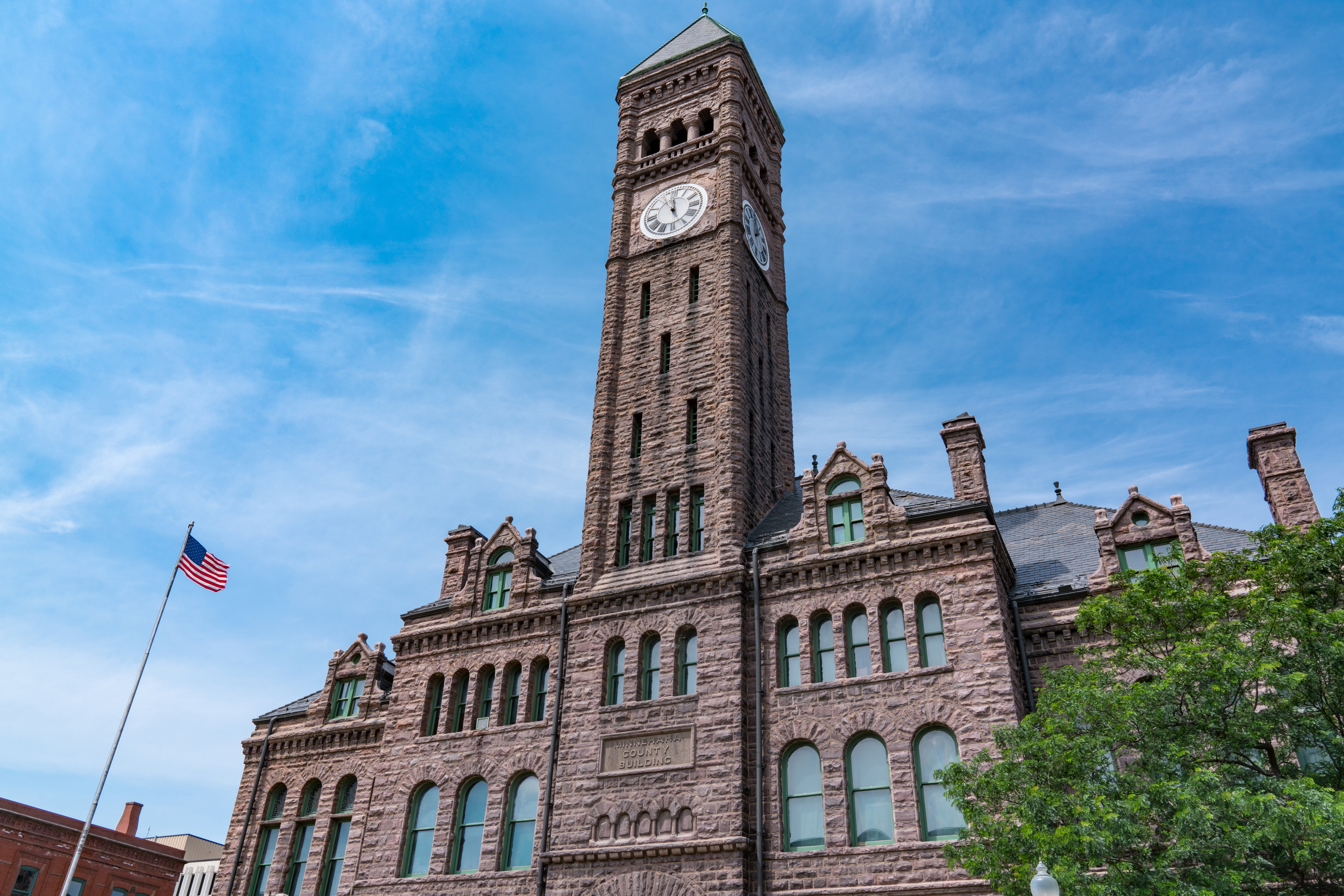 Historic Minnehaha County Building with stone clock tower and American flag in Sioux Falls, South Dakota.