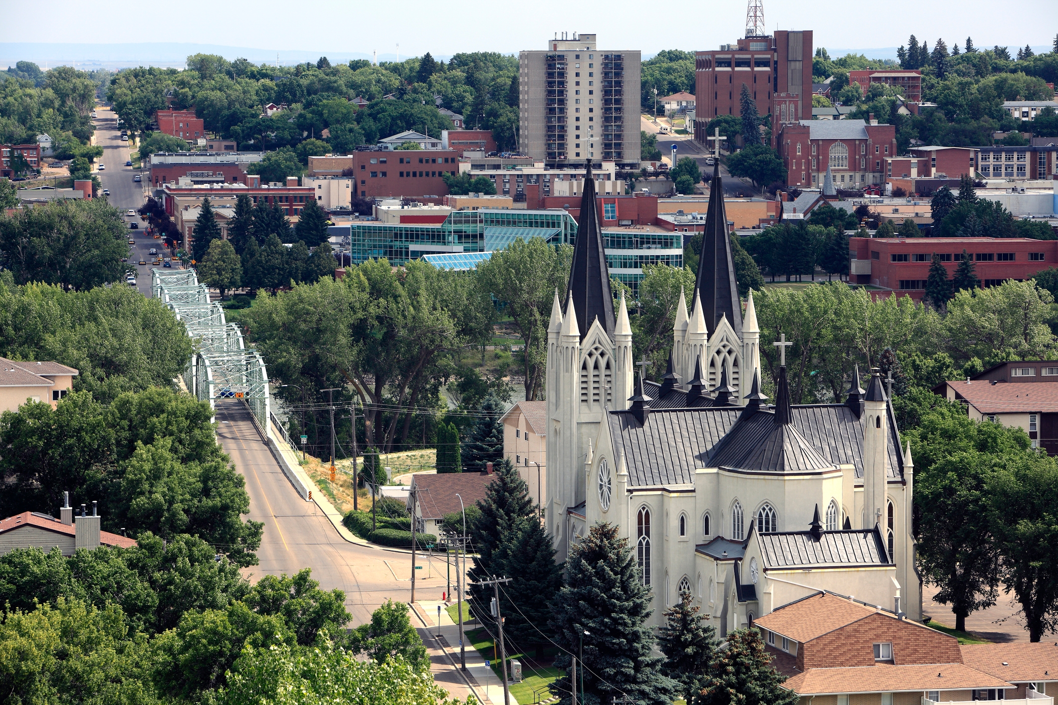 An elevated view of Medicine Hat, Alberta, featuring the striking twin spires of St. Patrick’s Church in the foreground, surrounded by lush greenery, residential neighborhoods, and downtown buildings in the distance.