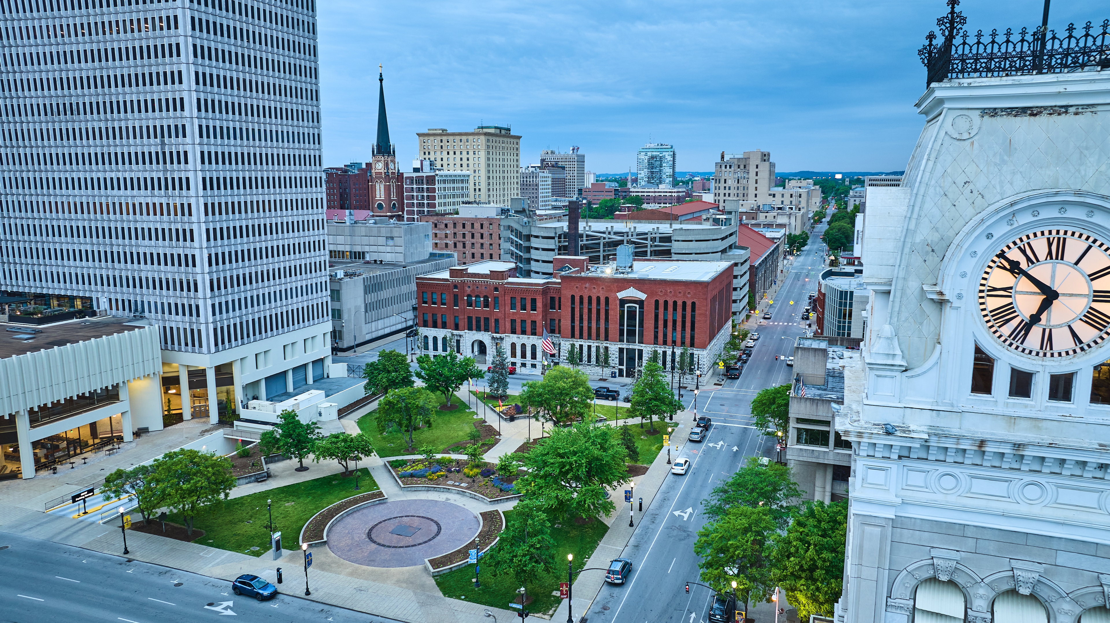 Downtown Louisville skyline at dusk with historic clock tower, city streets, and urban park.