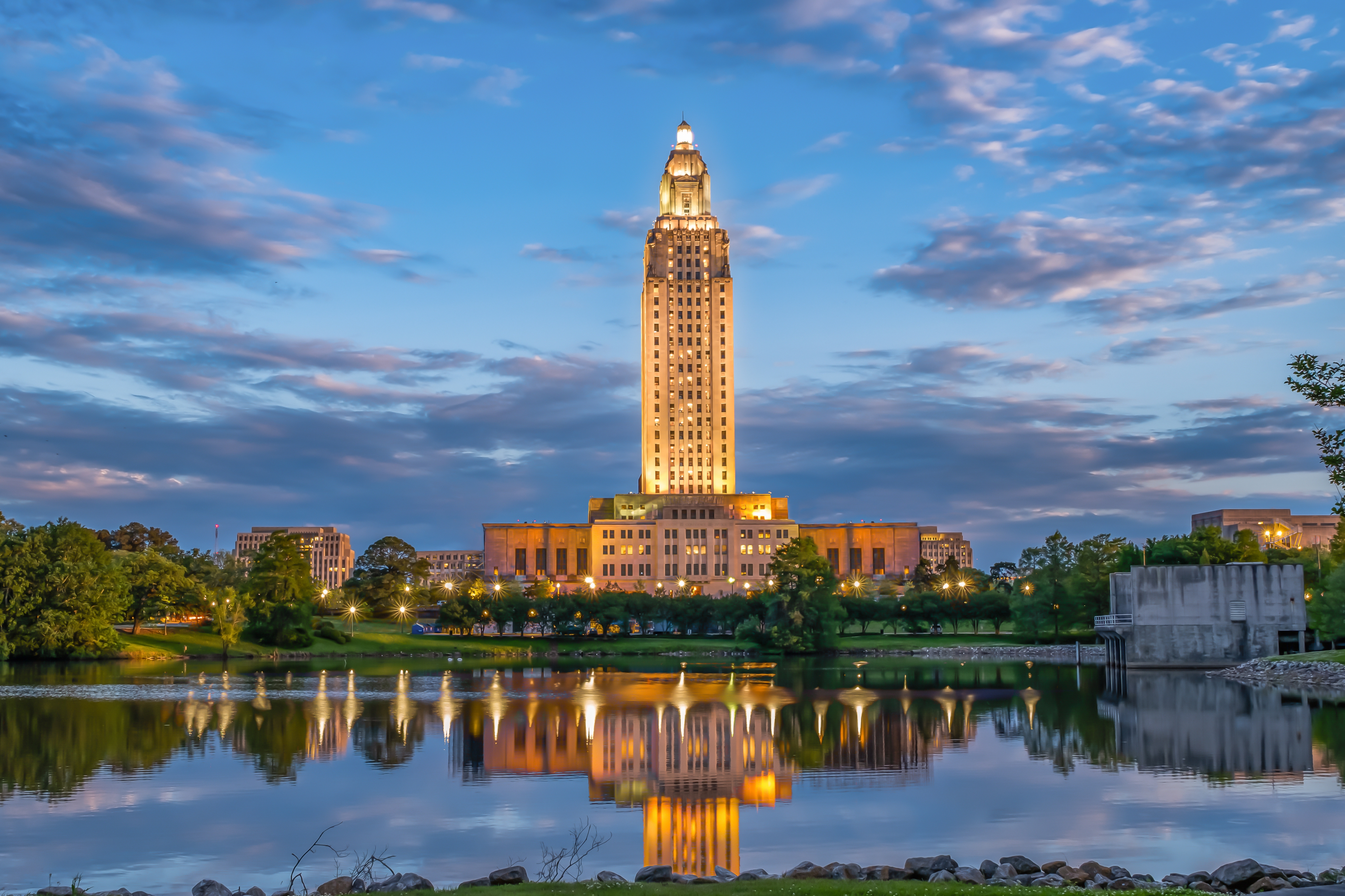 Twilight view of the Louisiana State Capitol in Baton Rouge, illuminated and reflected in the waters of Capitol Lake under a dramatic evening sky.