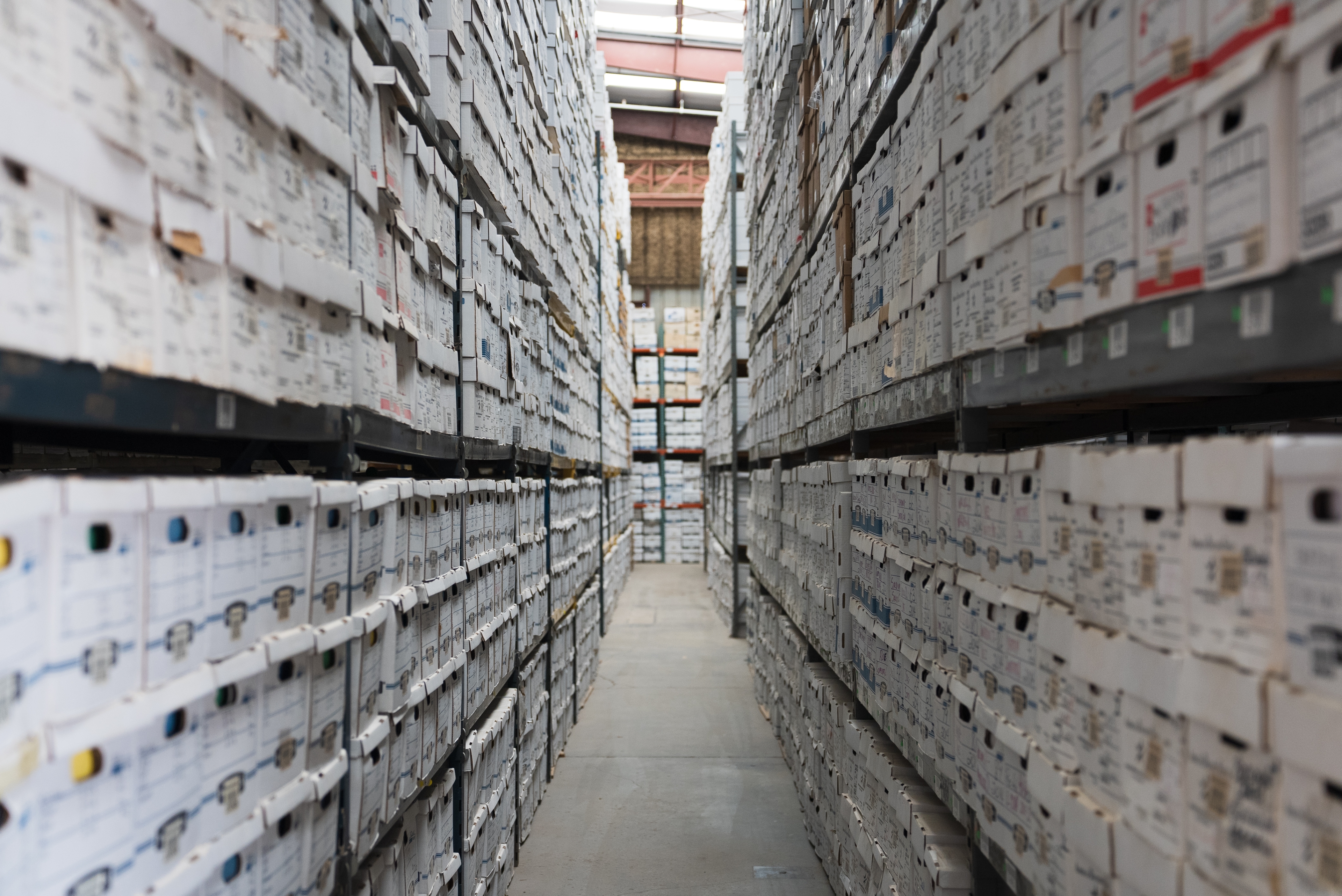 Narrow aisle in a records storage facility with shelves filled with white archival boxes.