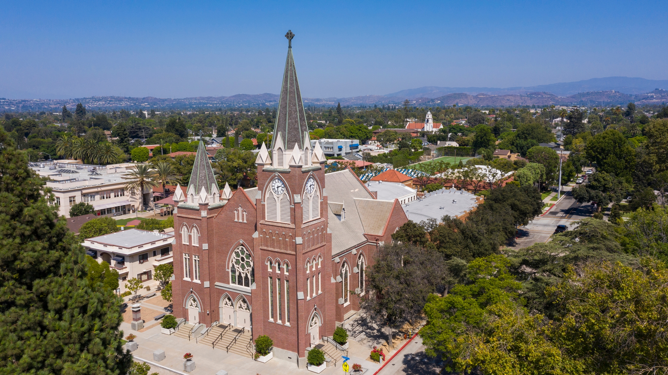 Aerial view of Holy Family Cathedral in Orange, California, featuring Gothic Revival architecture amid suburban neighborhoods and mountain backdrops.