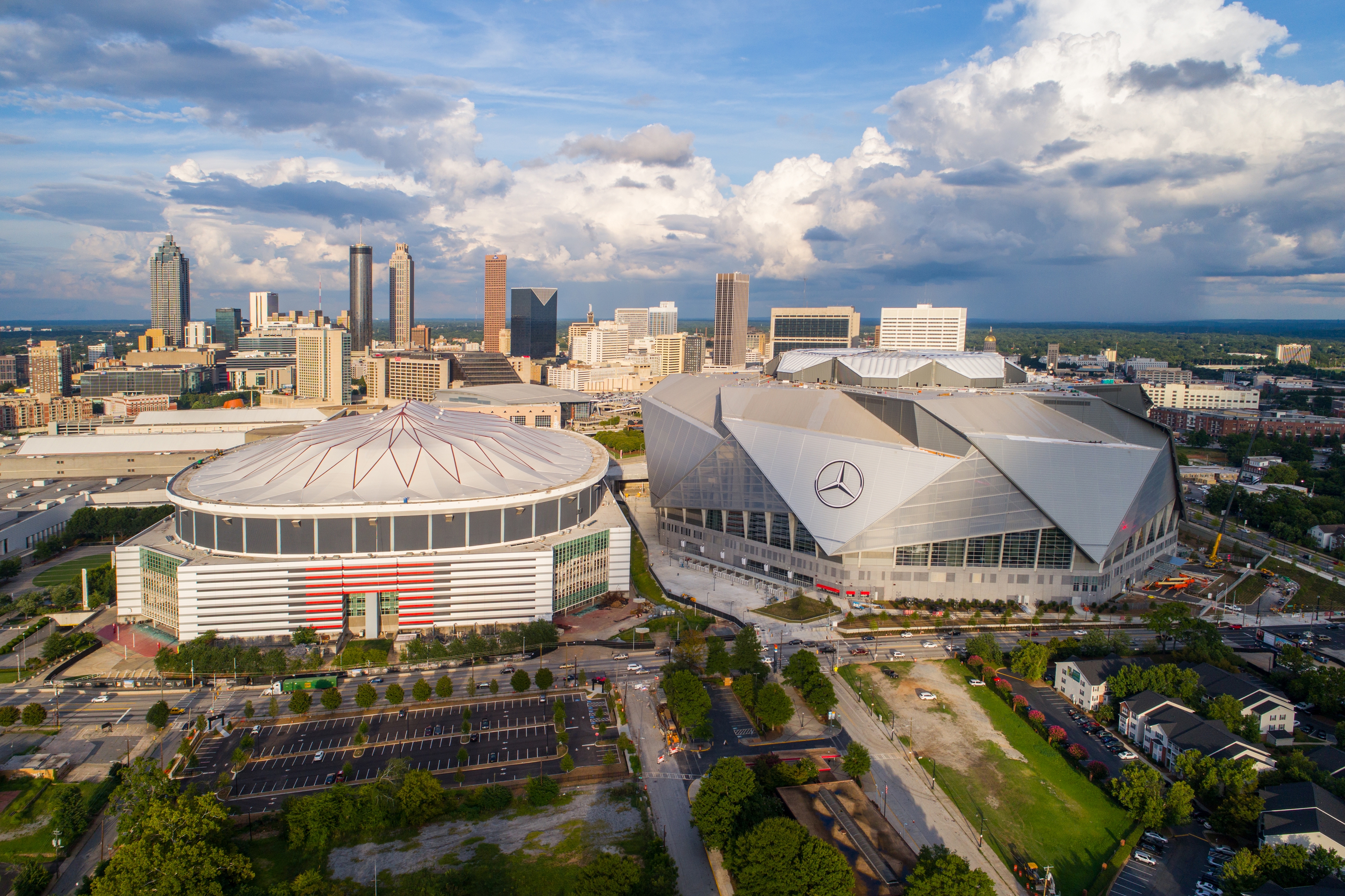 Aerial view of downtown Atlanta, showcasing the Mercedes-Benz Stadium, Georgia Dome, and surrounding skyscrapers under a partly cloudy sky.
