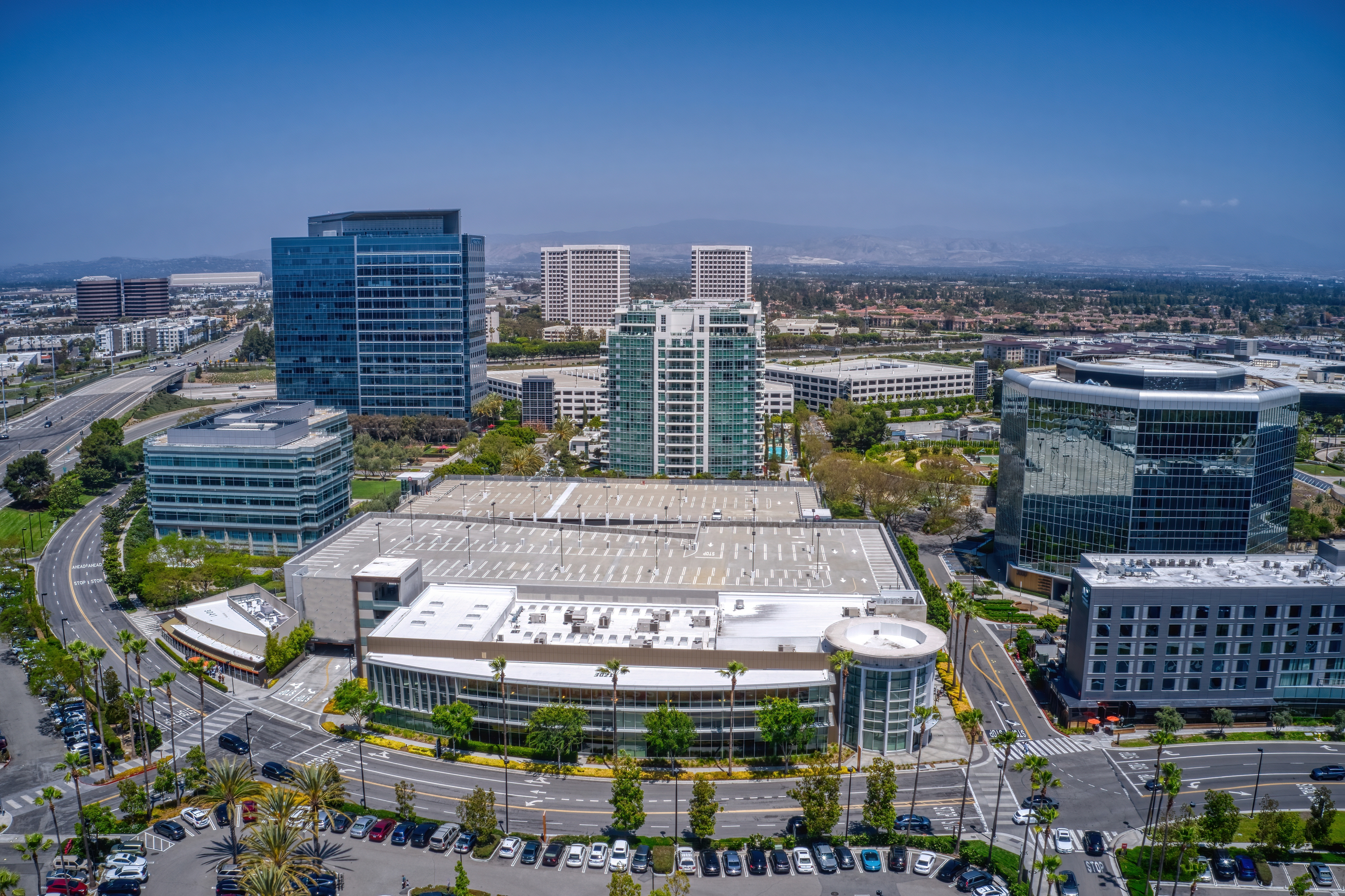 Aerial view of Irvine, California’s urban core, featuring modern office towers, commercial spaces, and major roadways under a clear blue sky.