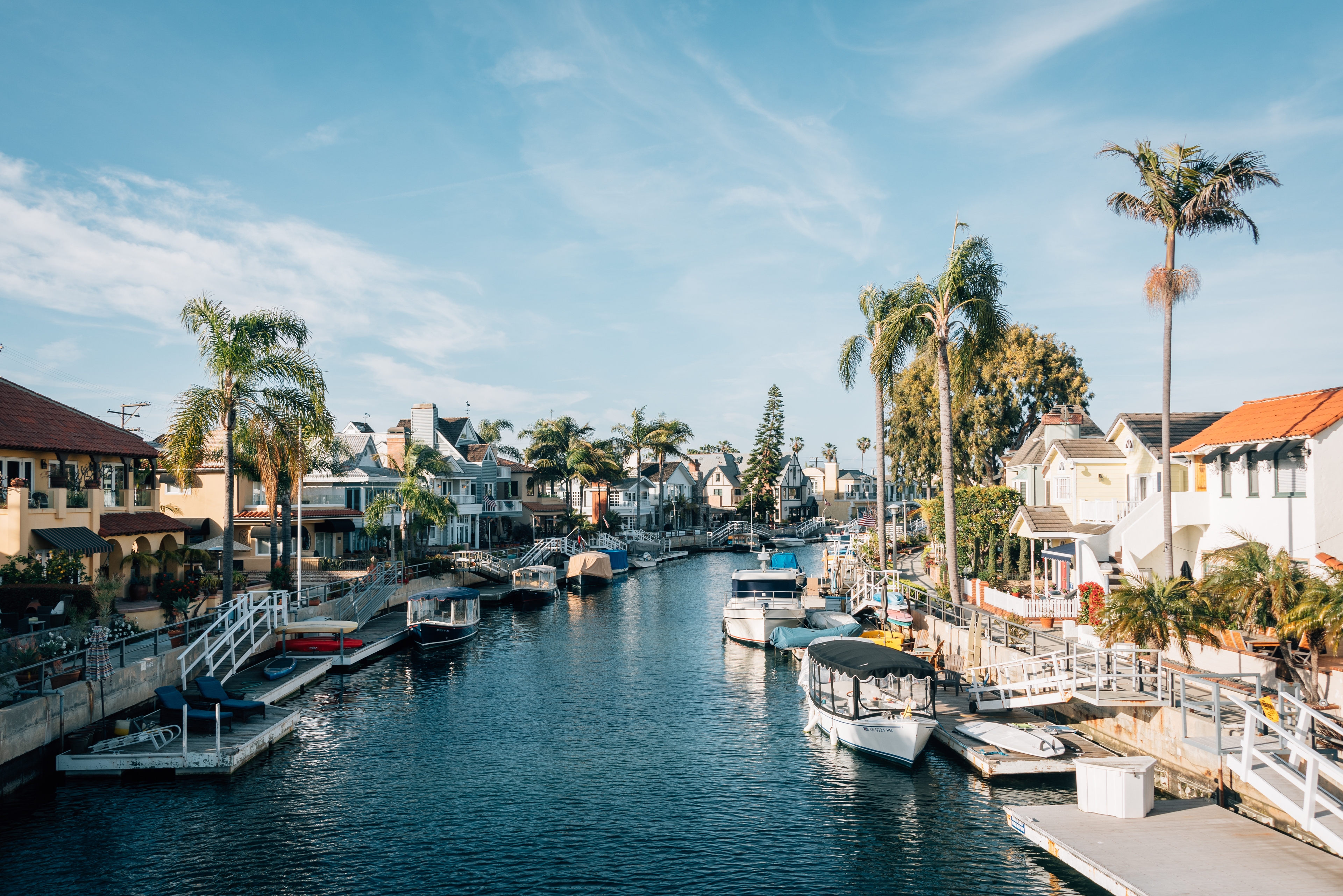 Beautiful Long Beach, California canal neighborhood featuring waterfront homes, docked boats, palm trees, and sunny blue skies. 