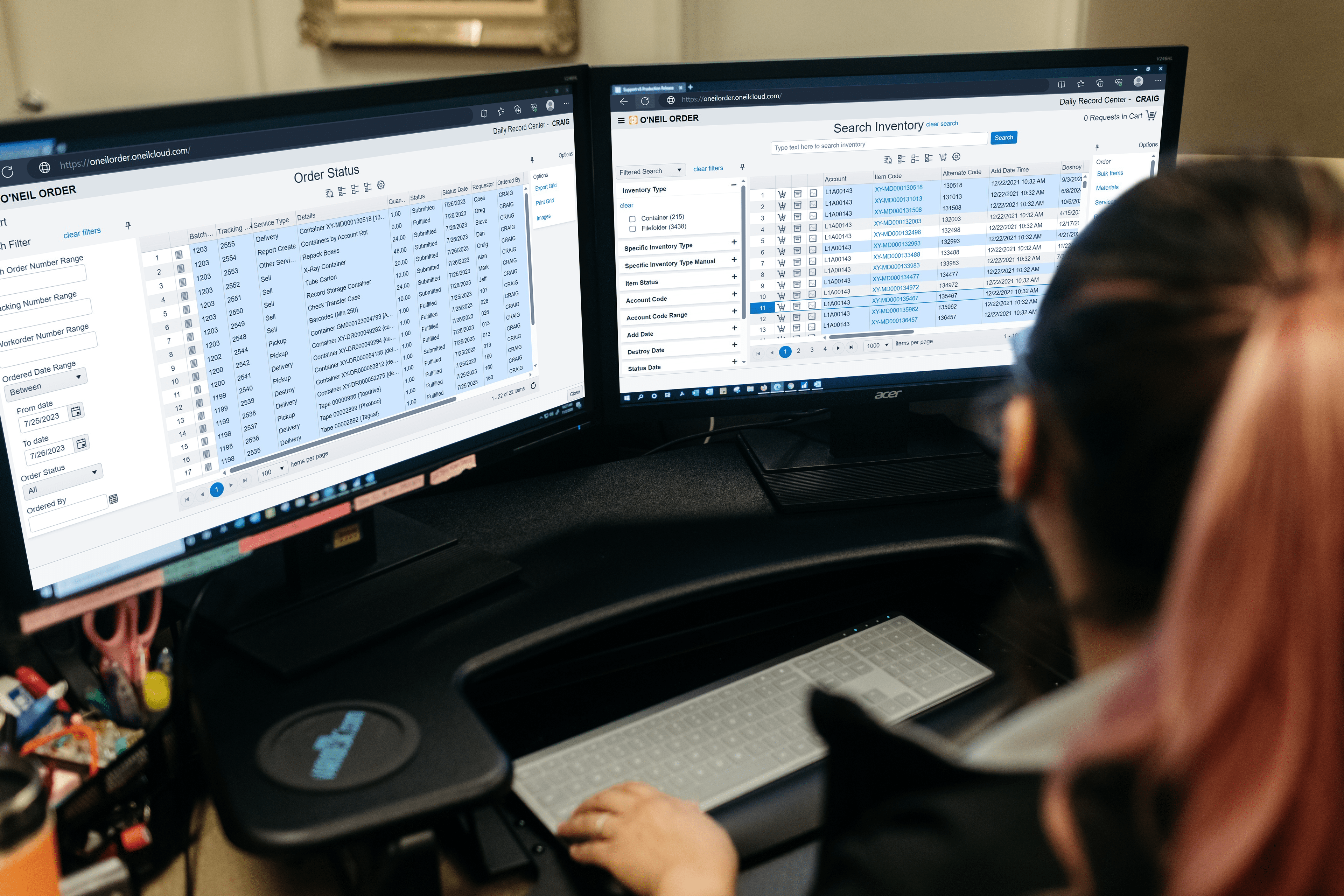 A person working at a dual-monitor setup displaying the O'Neil Order software. One screen shows an 'Order Status' page, while the other screen displays 'Search Inventory' results. The person is managing records or inventory in a structured software environment, suggesting a focus on efficient order and data tracking.