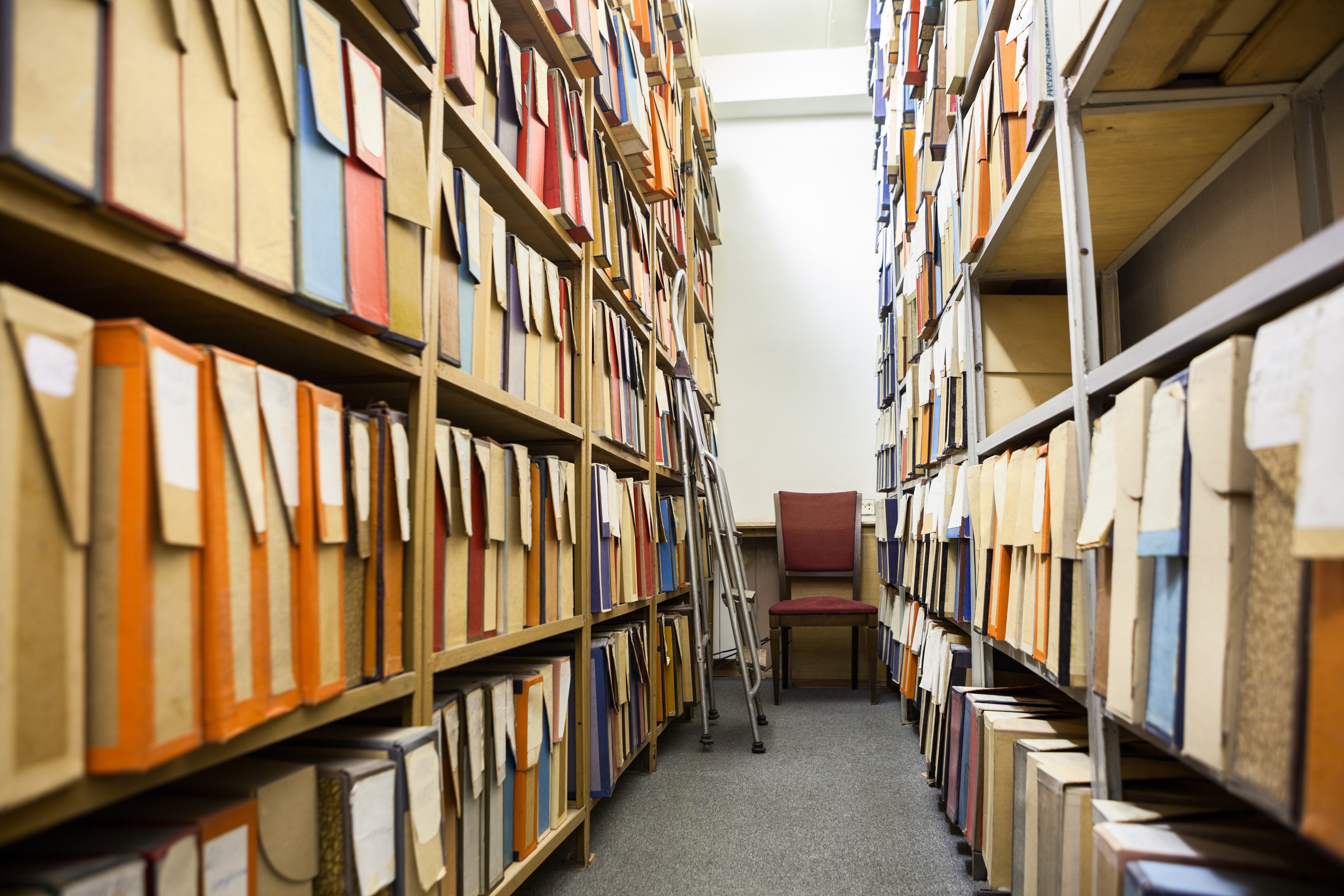 Archive room with shelves filled with colorful file boxes, a red chair, and a ladder.