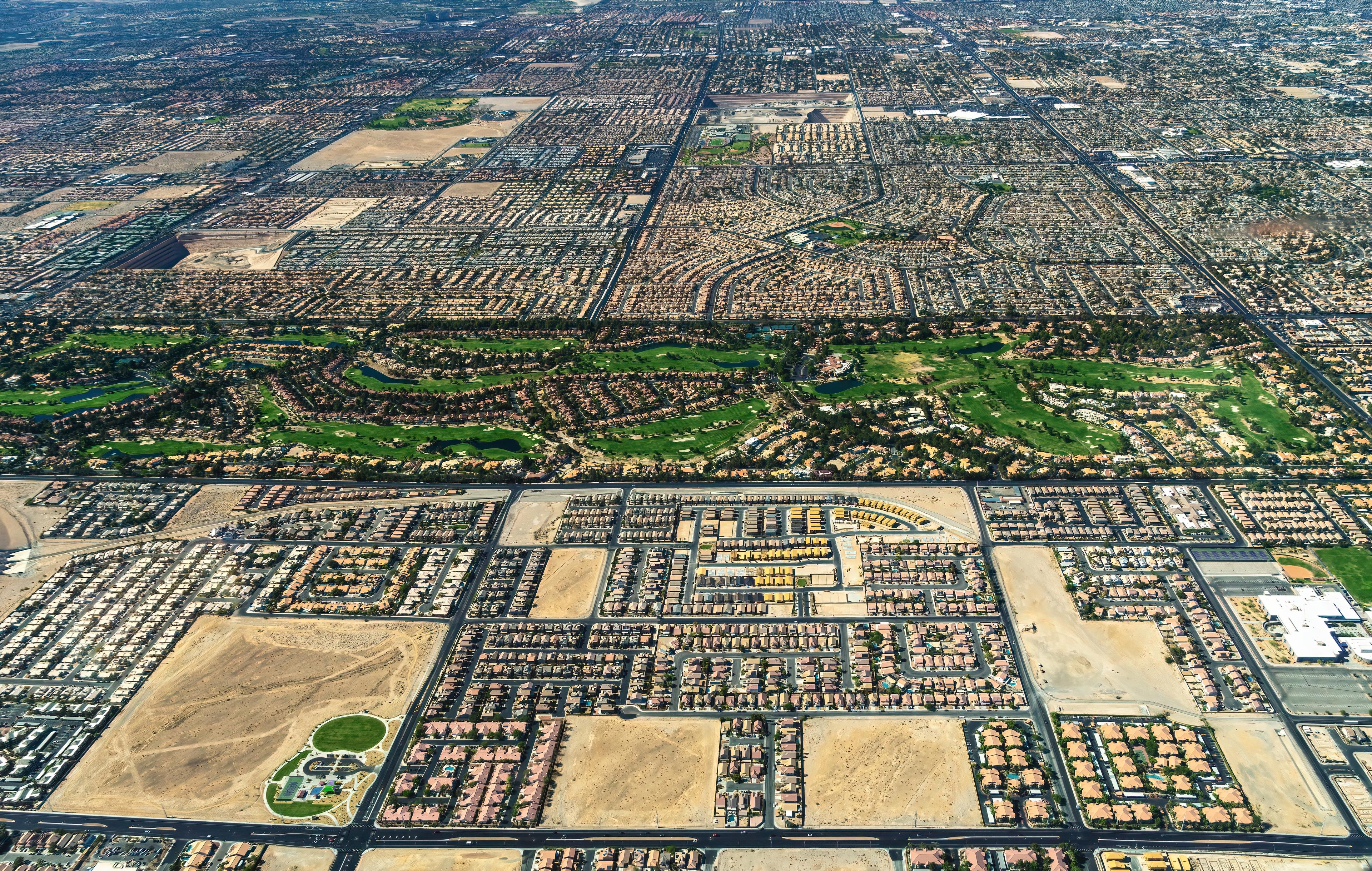 Aerial view of Henderson, Nevada showing sprawling suburban neighborhoods, desert terrain, and a lush golf course cutting through the landscape.
