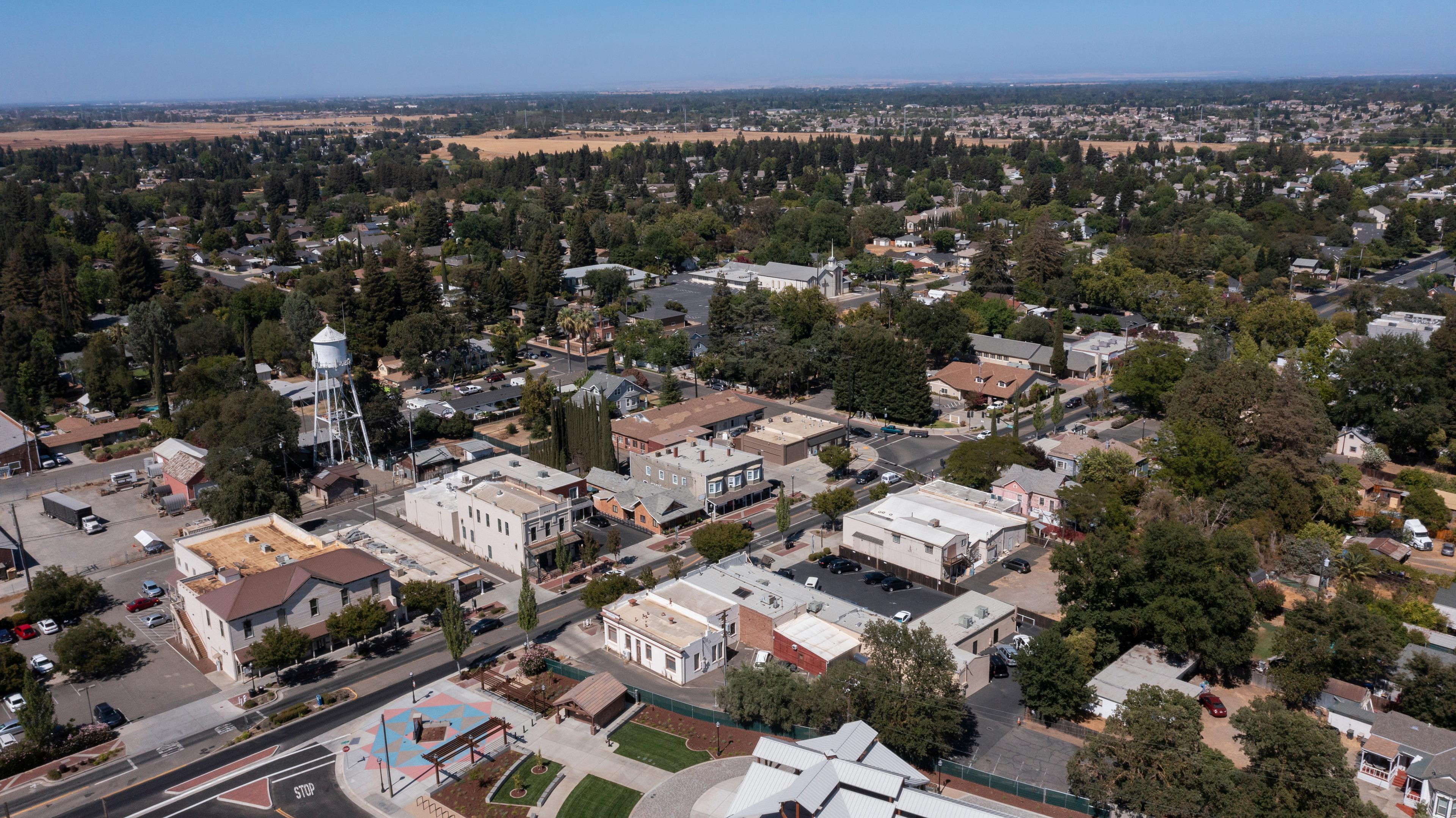 An aerial view of Elk Grove, California, showcasing a mix of residential neighborhoods, a historic water tower, and tree-lined streets under a bright blue sky.