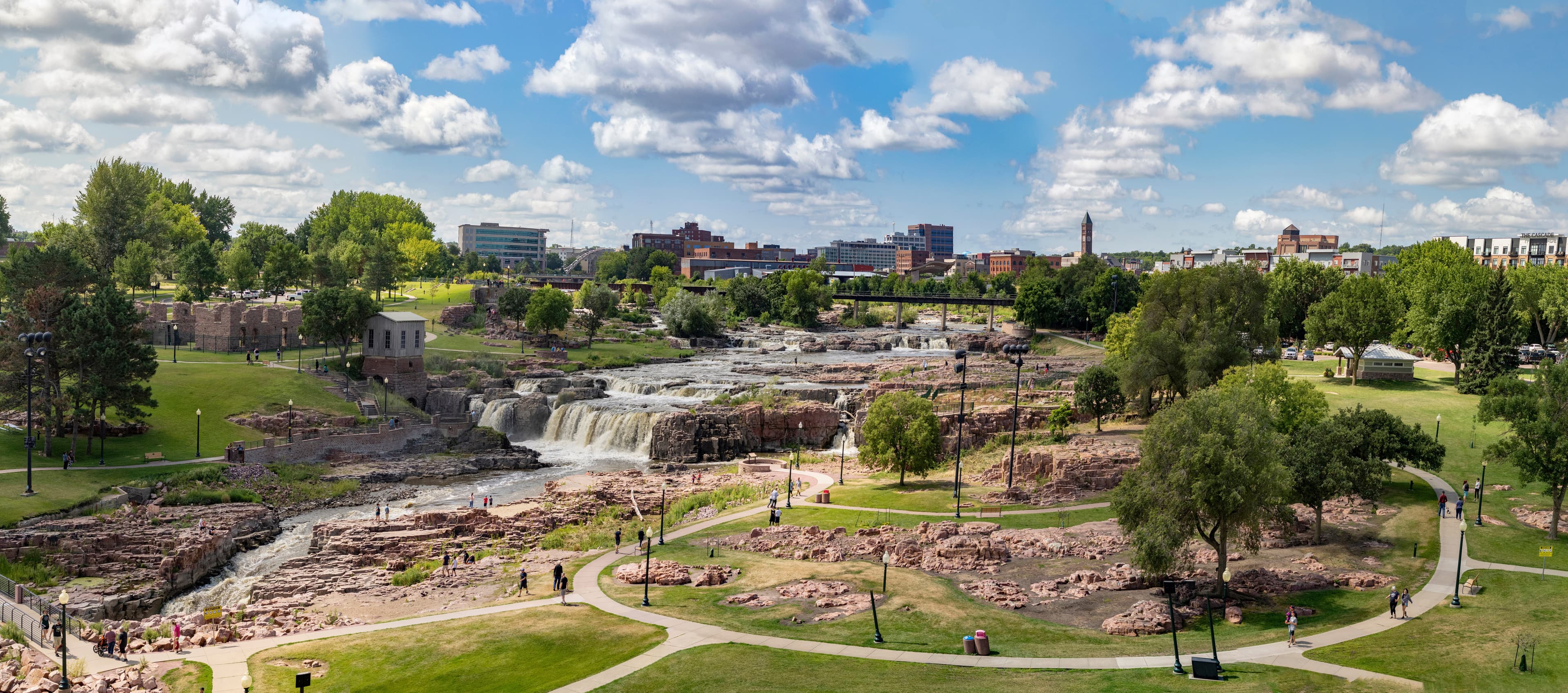 Falls Park waterfalls and downtown Sioux Falls, South Dakota, with walking paths, green space, and the city skyline.