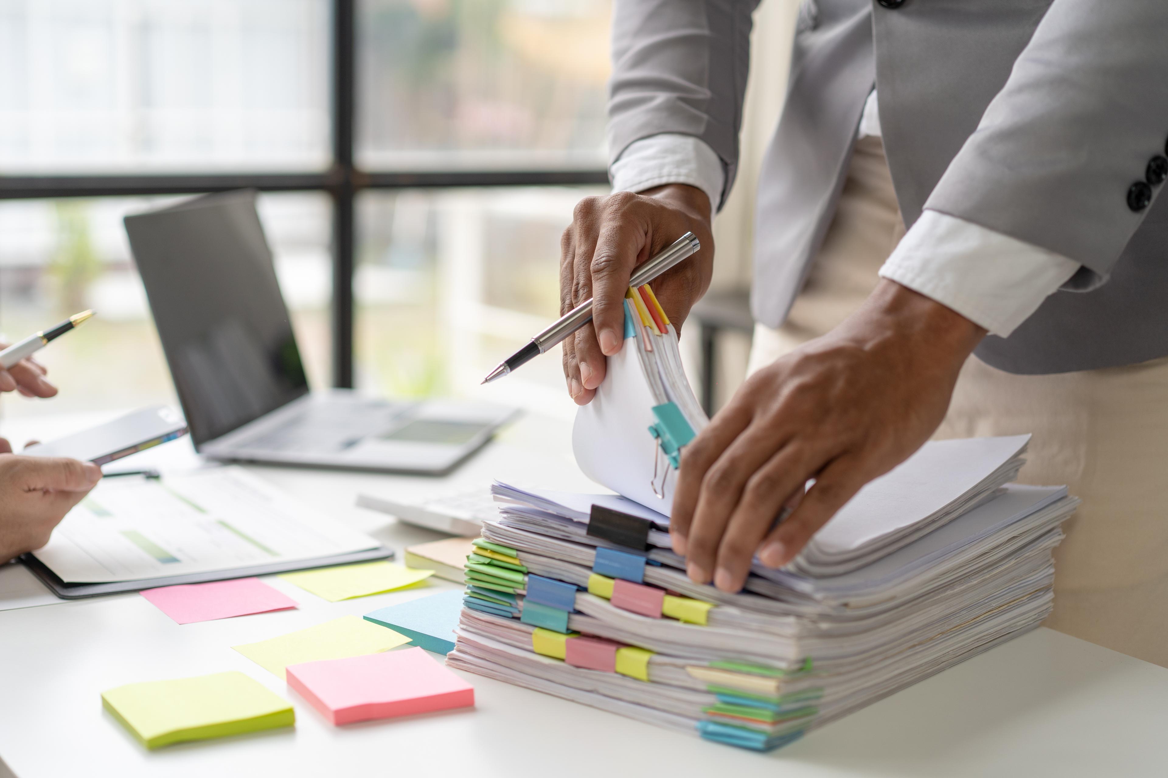 Two financial workers collaborating on a stack of organized financial records, managing their stored records on the Annex platform on their phones. 