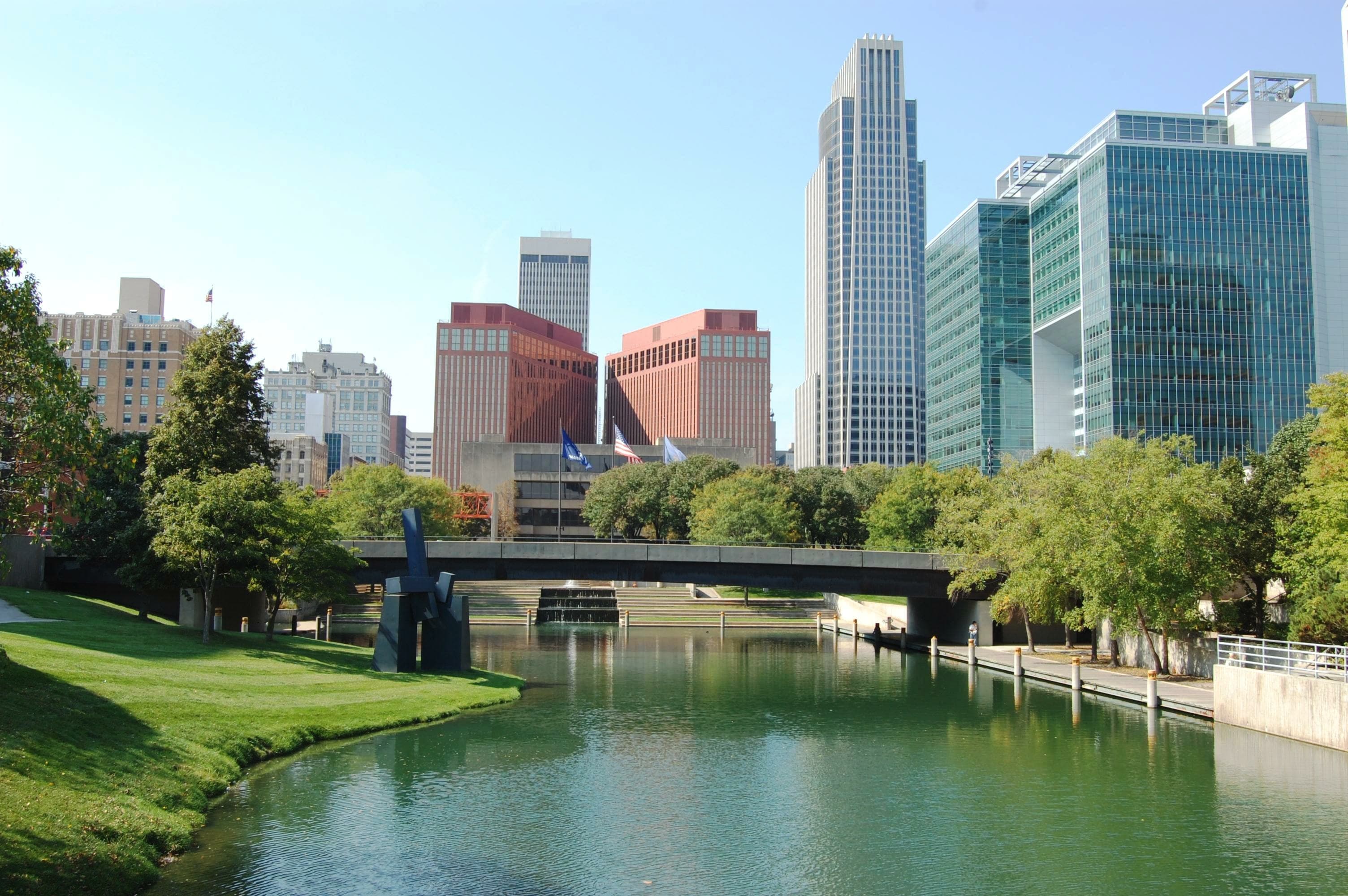 Downtown Omaha, Nebraska skyline with modern office buildings, green park space and a reflecting lagoon on a sunny day.