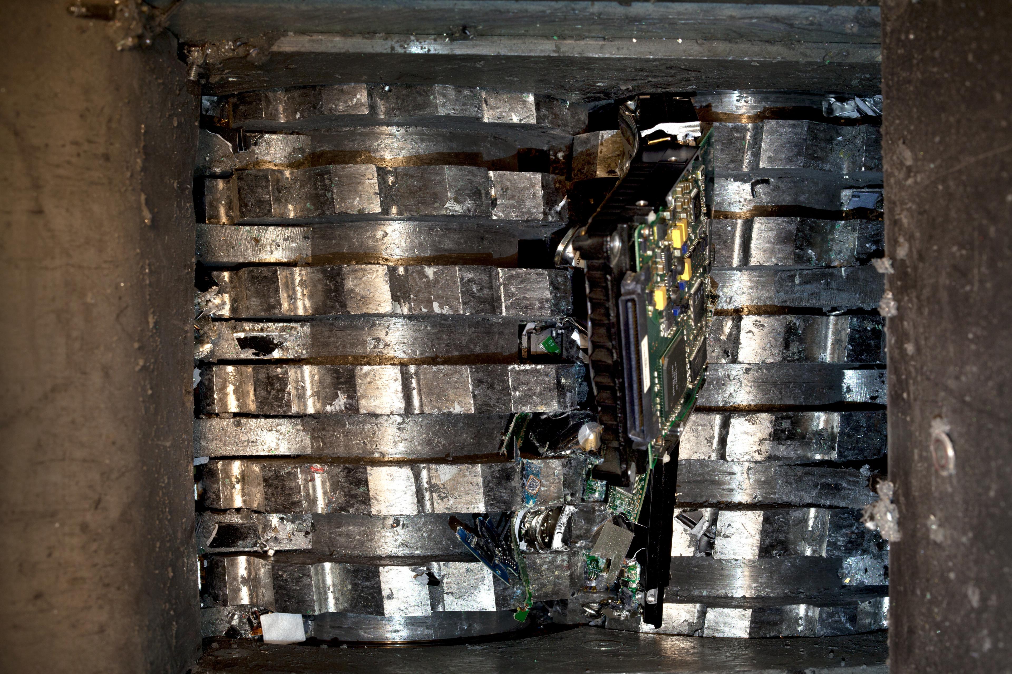 A hard drive is destroyed in an industrial shredder, illustrating the physical data destruction process for secure IT asset disposal and compliance.