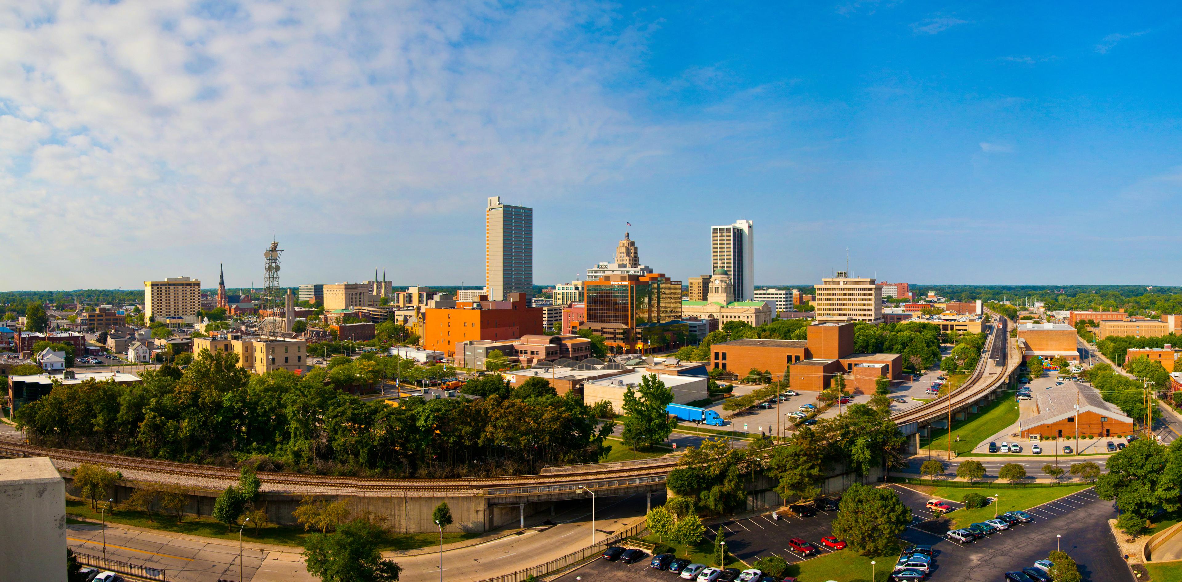 Panoramic view of downtown Fort Wayne, Indiana on a clear day, showcasing the city skyline, rail lines, and a mix of modern and historic architecture.