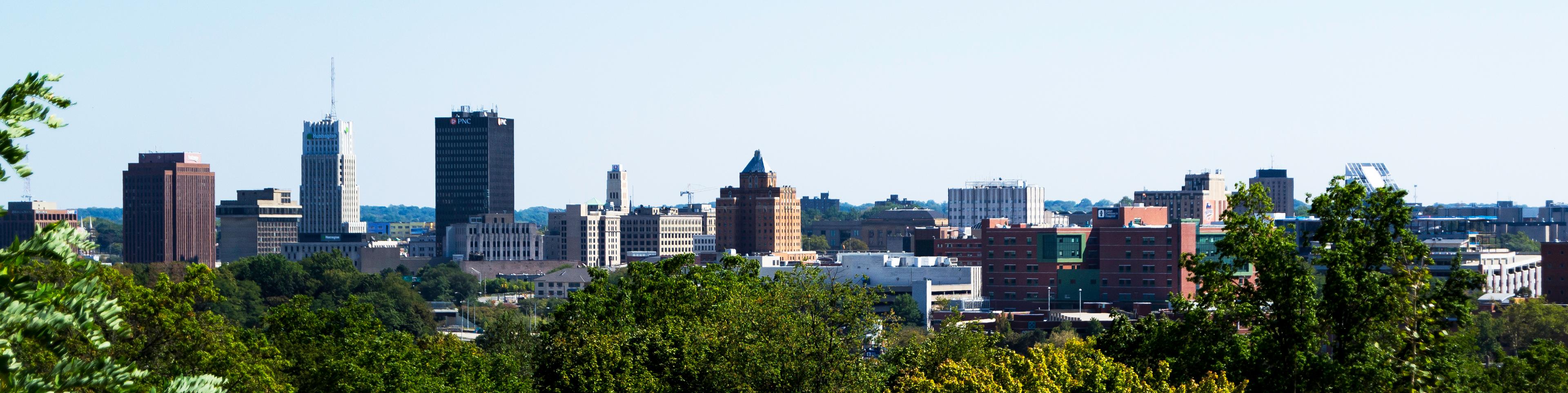 Panoramic view of the Akron, Ohio skyline, showcasing a mix of historic and modern buildings under a clear blue sky. 