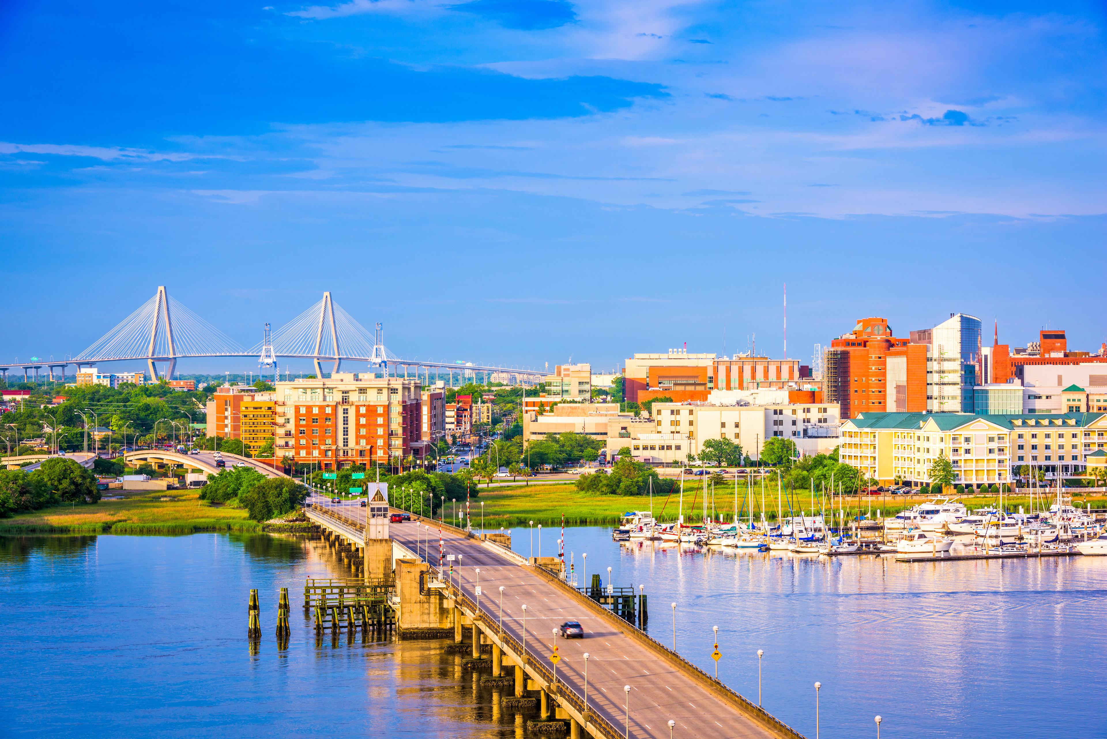 Colorful view of downtown Charleston, South Carolina, with the Arthur Ravenel Jr. Bridge in the background and a marina full of boats reflecting on the water in the foreground.