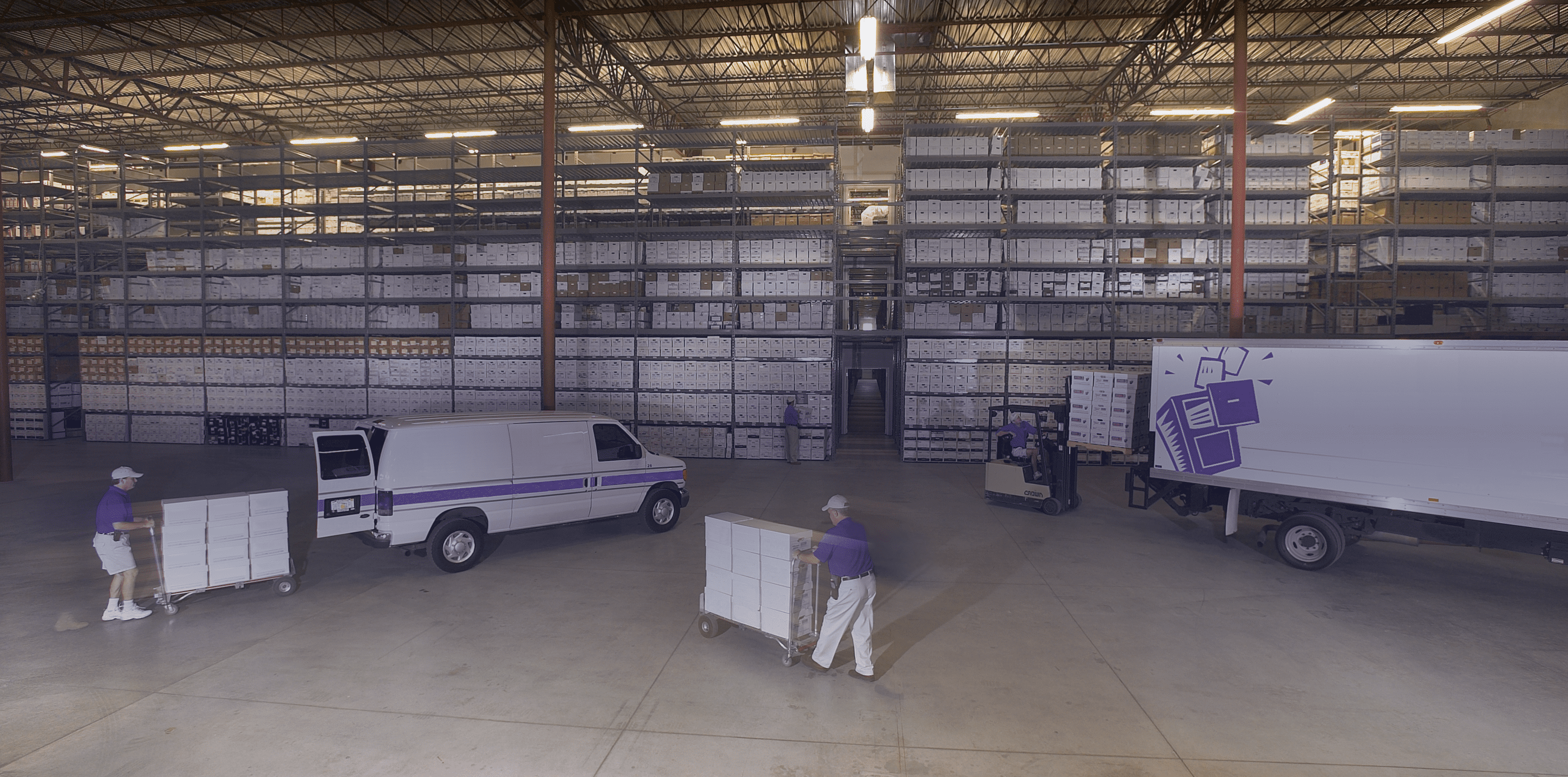 A busy records management warehouse with workers transporting document storage carts between trucks and shelves.