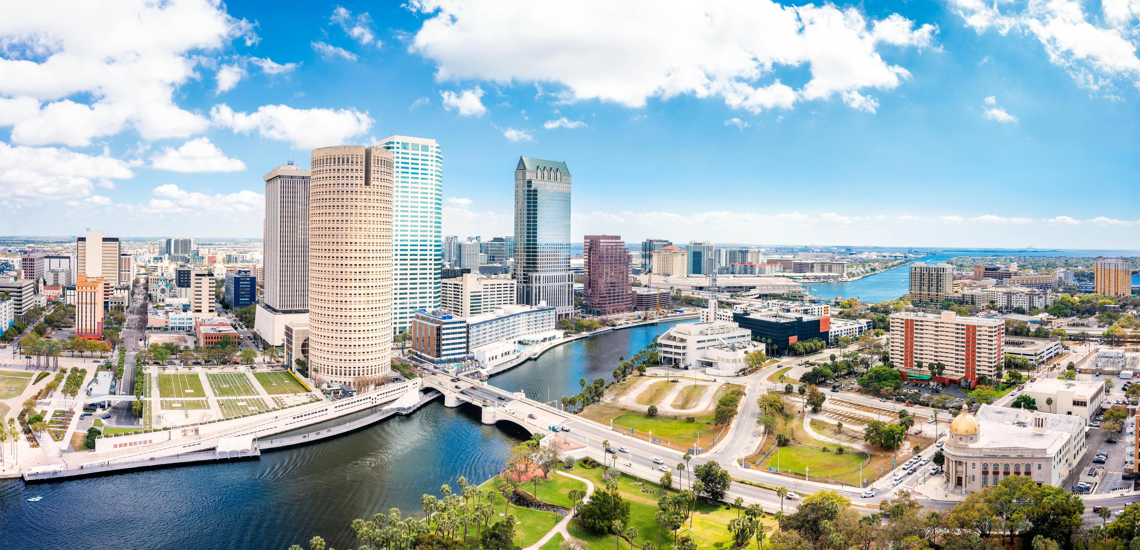 Panoramic aerial view of downtown Tampa featuring the Hillsborough River, high-rise buildings, and waterfront green spaces on a sunny day.