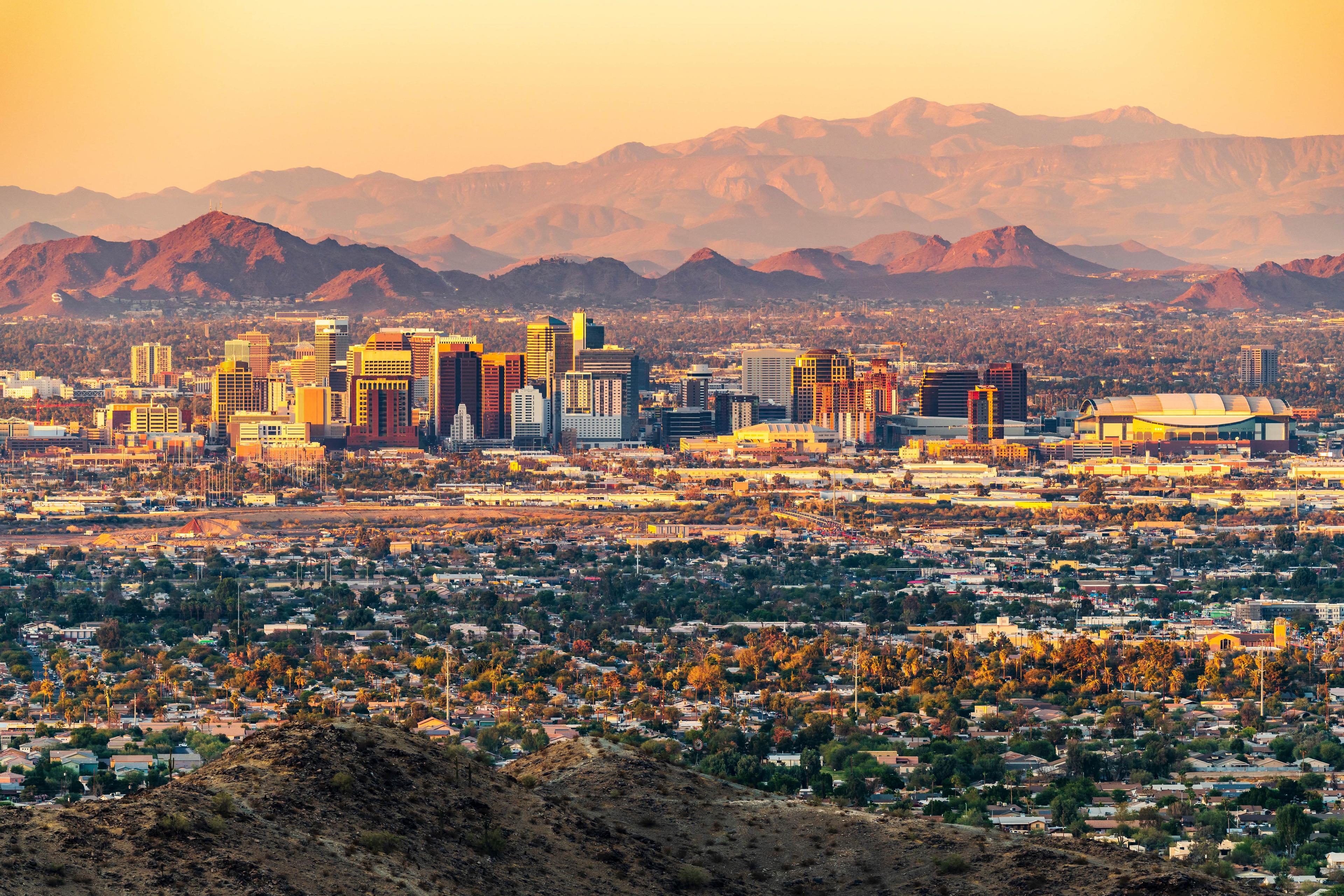 Panoramic view of downtown Phoenix, Arizona at sunset with mountains in the background and urban sprawl in the foreground.

