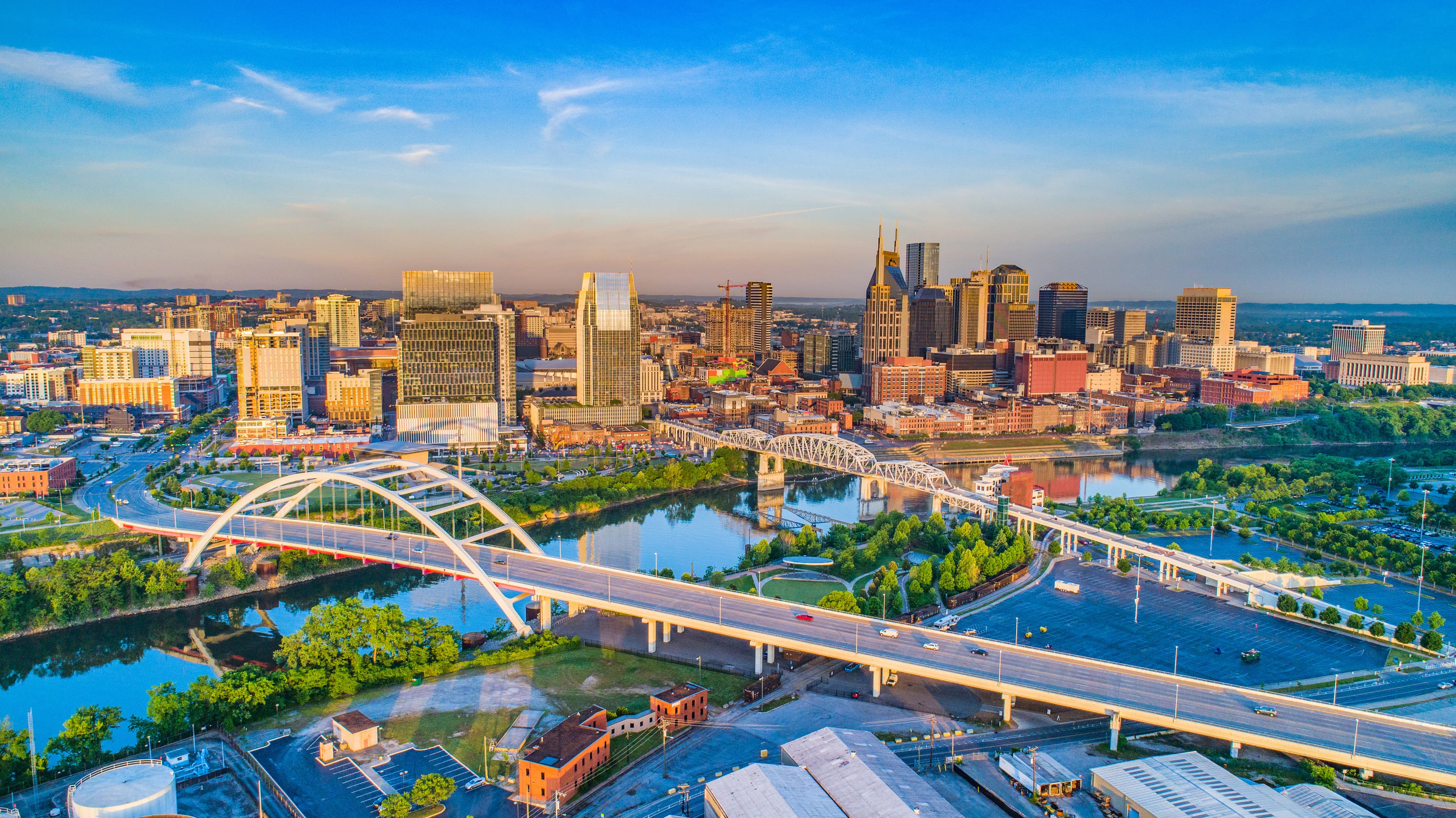 Nashville skyline at sunrise with bridges crossing the Cumberland River and downtown cityscape.