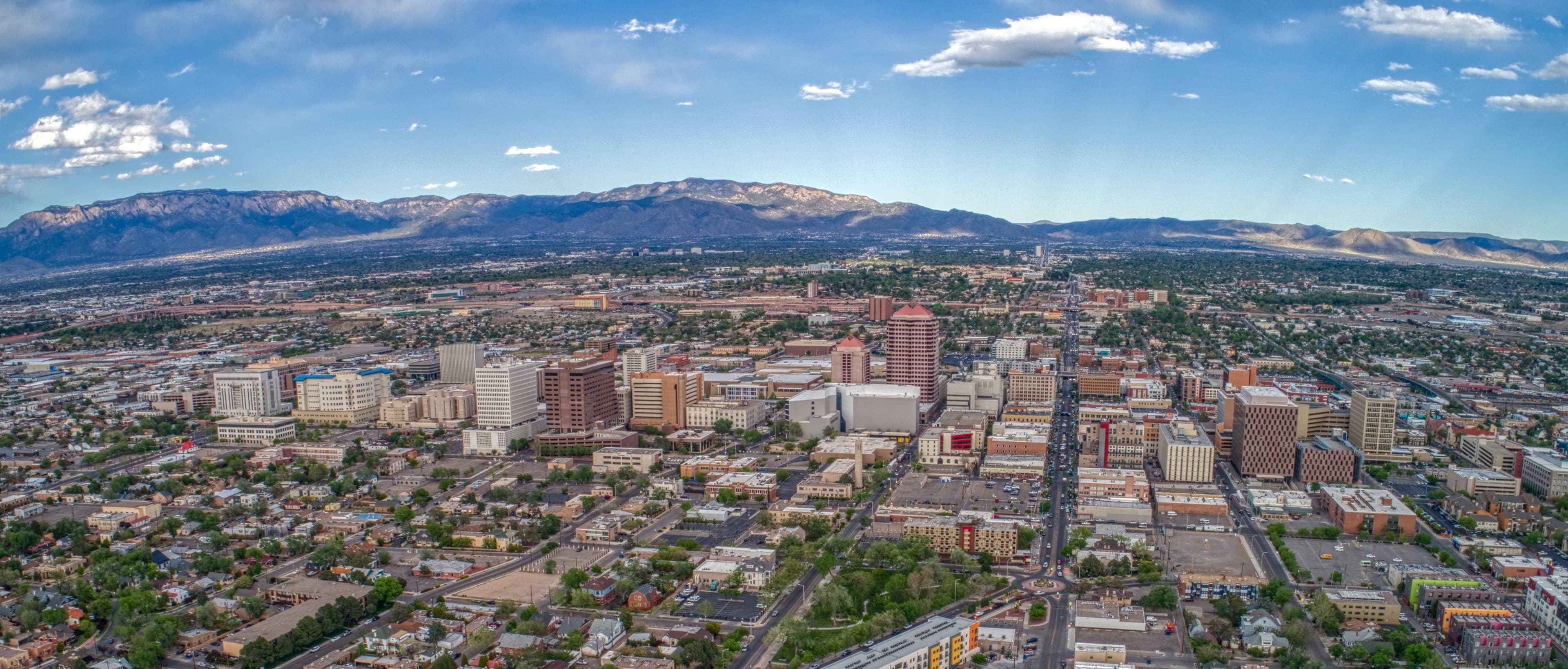 Albuquerque skyline with downtown buildings and Sandia Mountains under a bright blue sky.