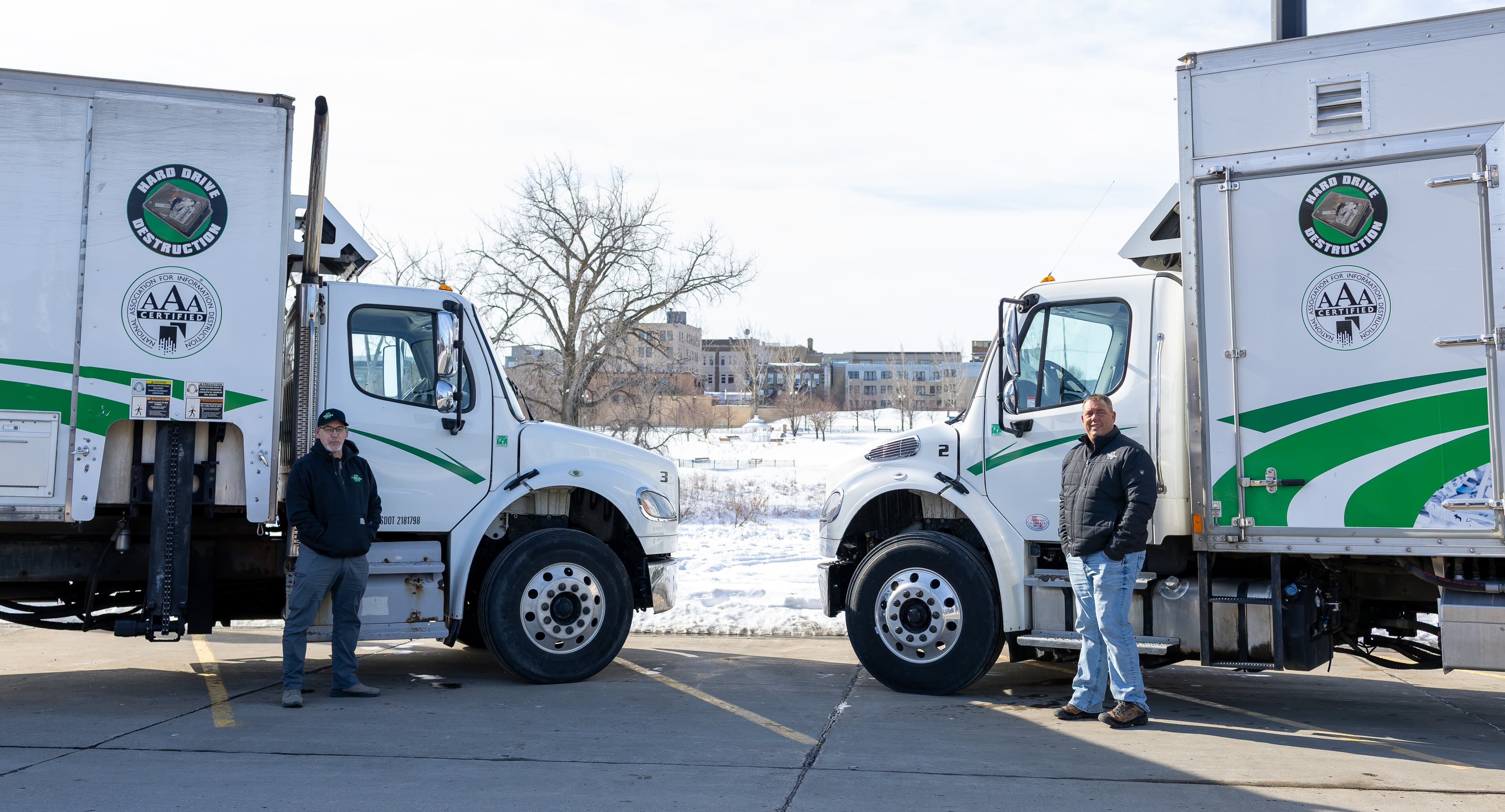 Two secure shredding trucks with certified hard drive destruction services parked side by side, with operators standing beside vehicles