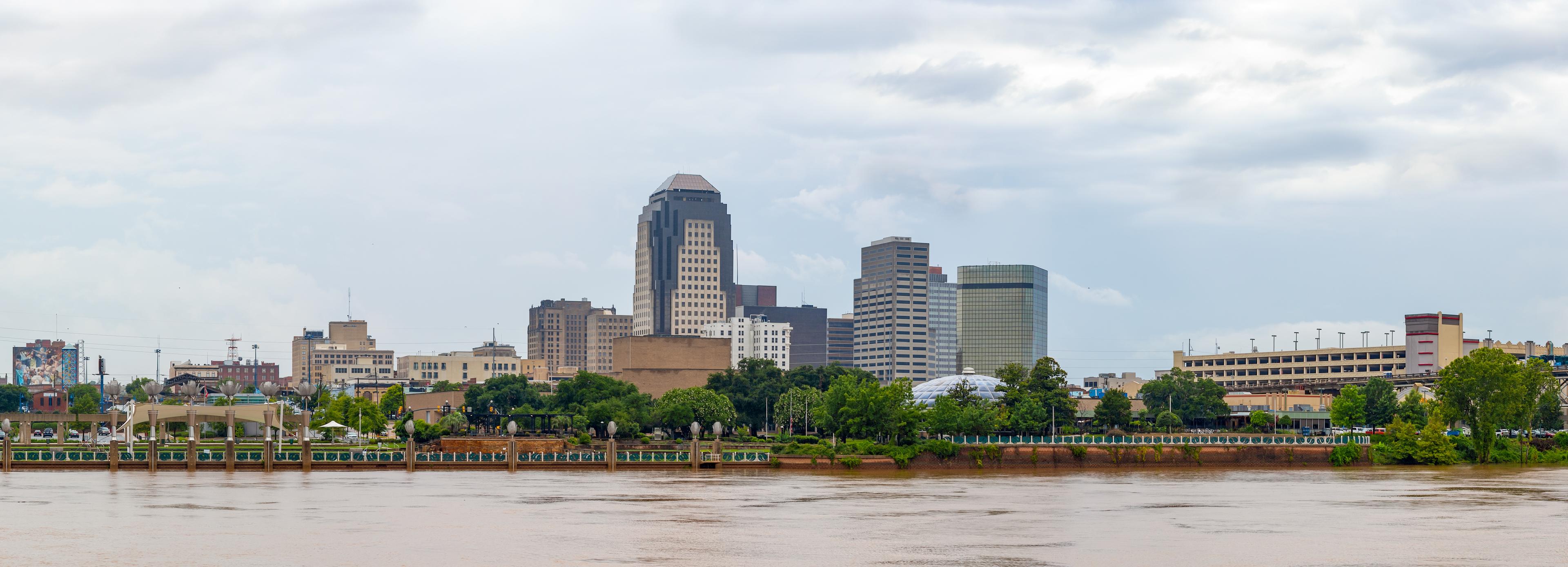Panoramic view of downtown Shreveport, Louisiana on an overcast day, with the city skyline rising behind the Red River and waterfront promenade.