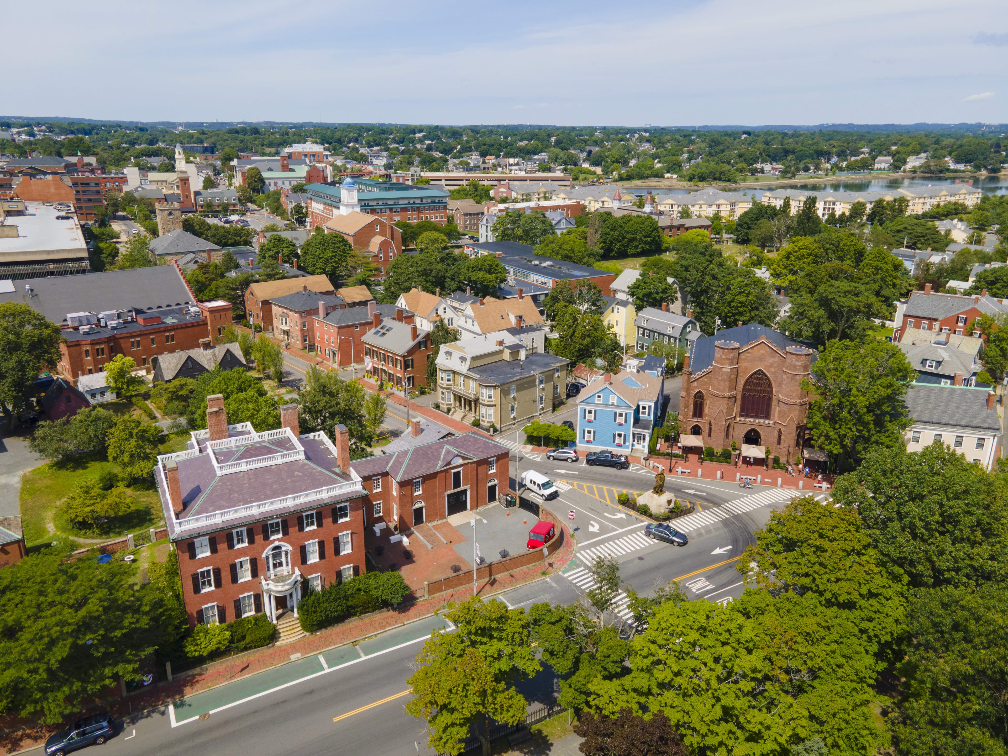 Aerial view of historic downtown Salem, Massachusetts, showcasing brick colonial-style buildings, churches, tree-lined streets, and vibrant homes on a sunny day.