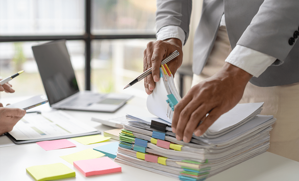 Two financial workers collaborating on a stack of organized financial records, managing their stored records on the Annex platform on their phones. 