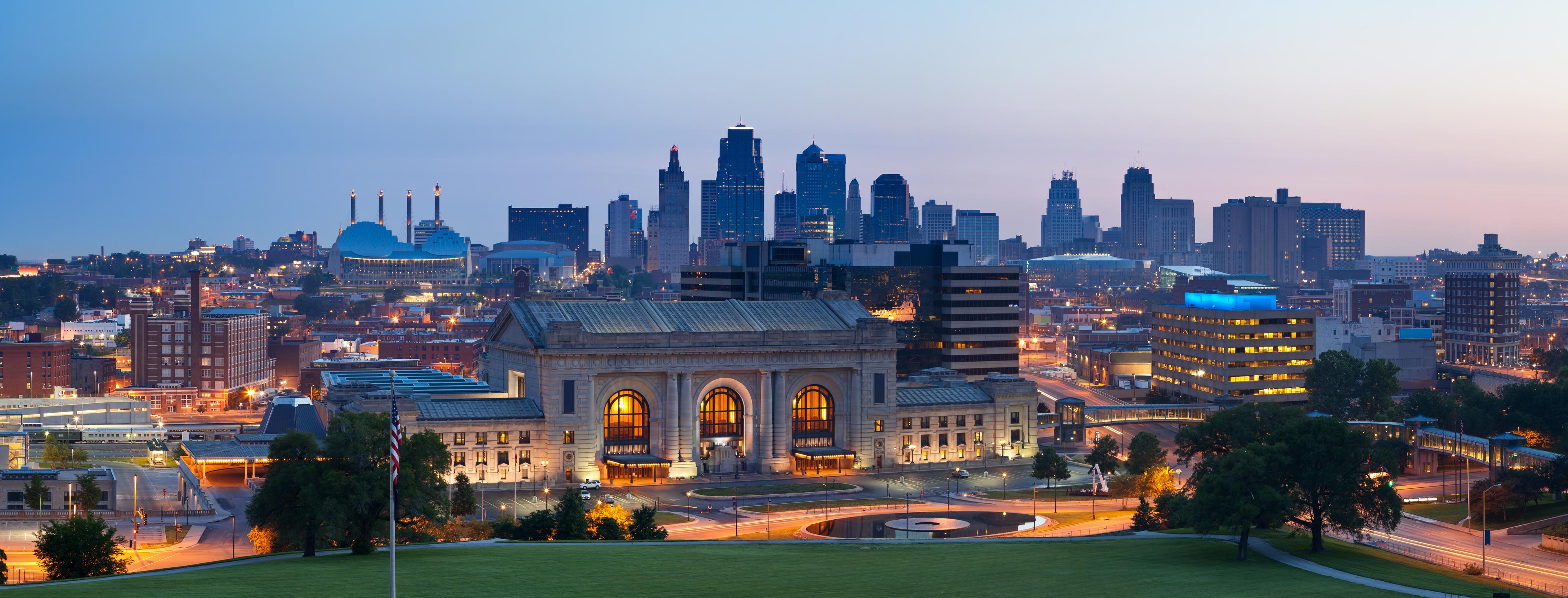 Panoramic view of downtown Kansas City at dusk featuring Union Station in the foreground, glowing city lights, and the illuminated skyline under a twilight sky.