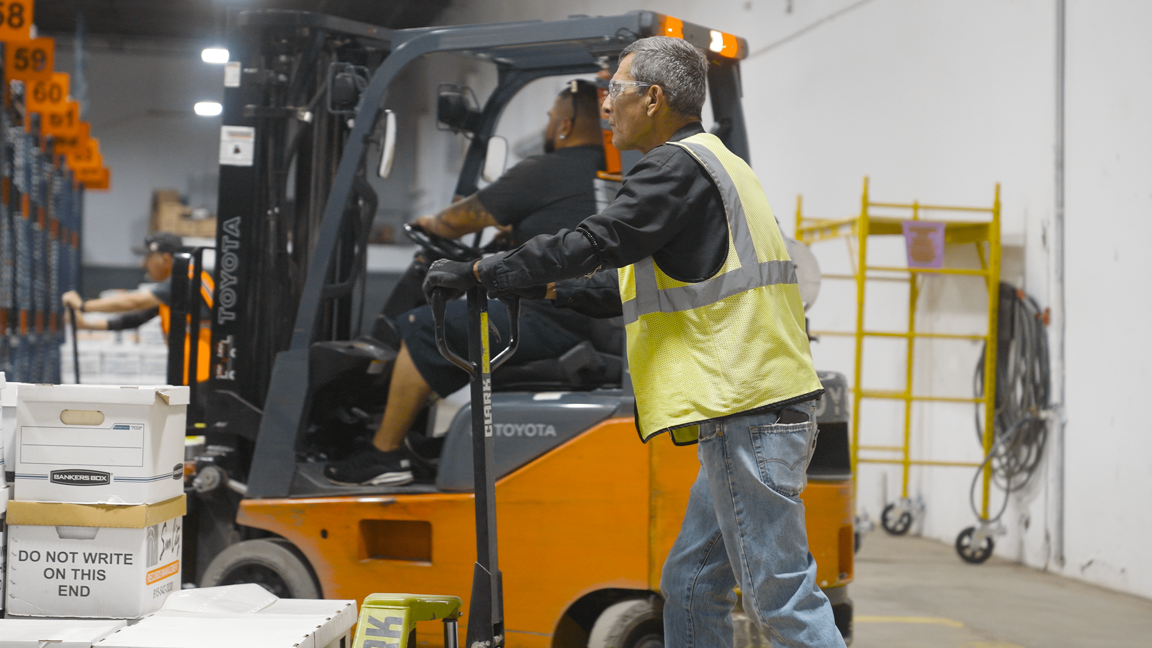 Employees in a secure records management facility organize and transport document storage boxes, ensuring efficient handling and retrieval in a high-volume warehouse.