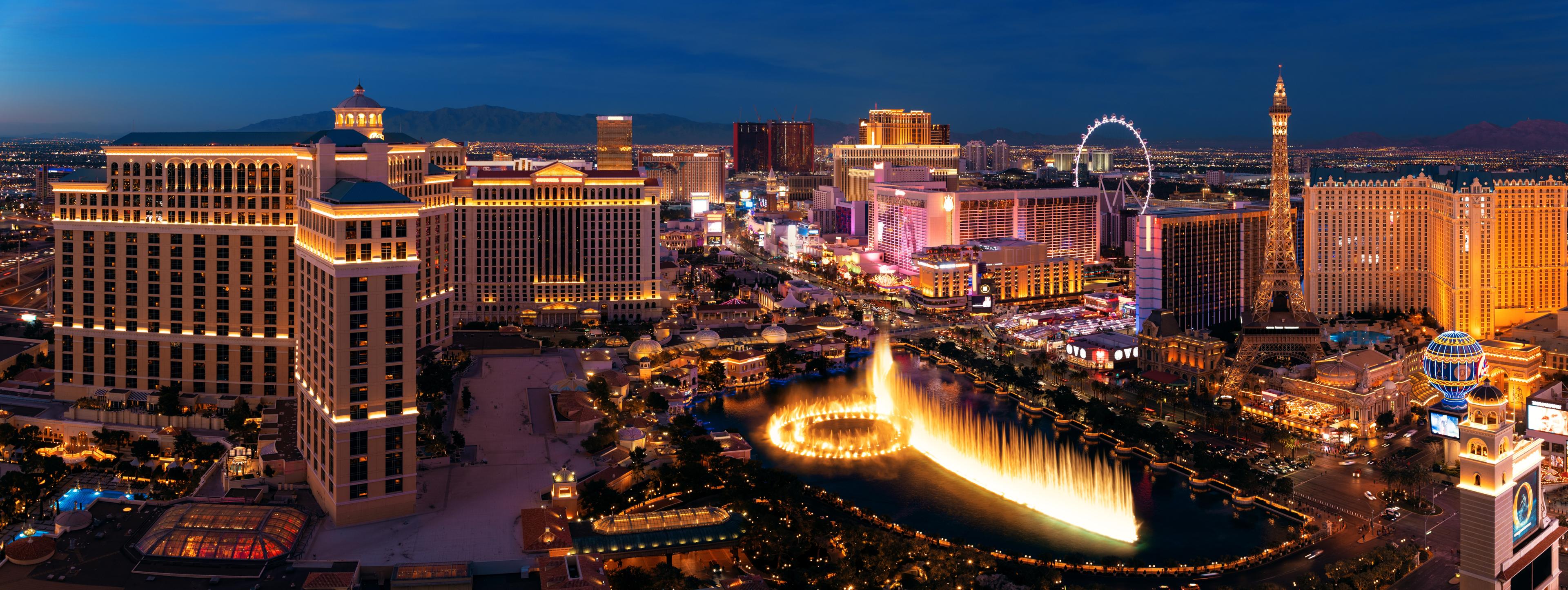 Panoramic view of the Las Vegas Strip at night featuring the Bellagio fountains, illuminated hotels, and iconic landmarks like the Eiffel Tower replica.