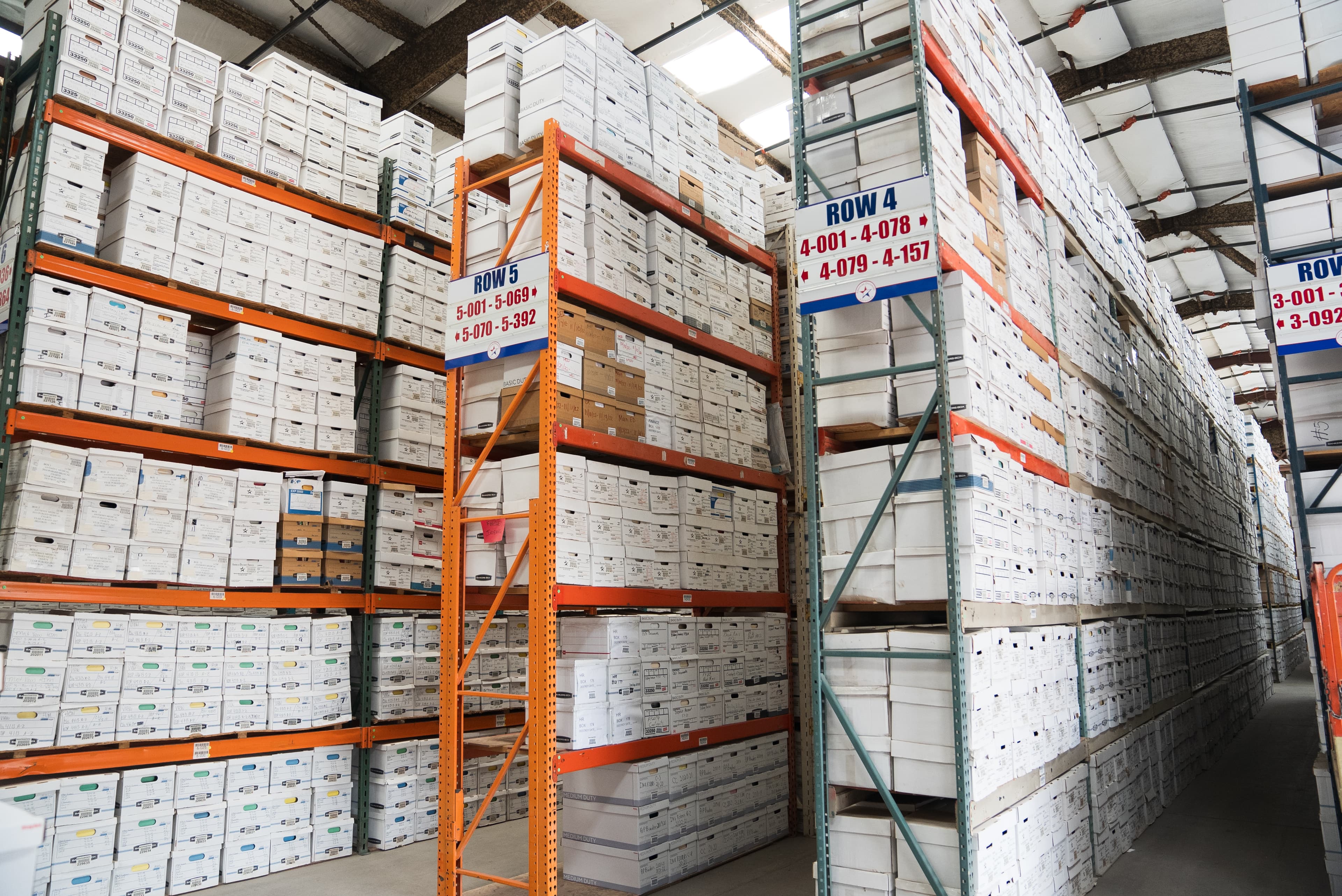 High-density warehouse shelving filled with labeled white document storage boxes organized by row and section.