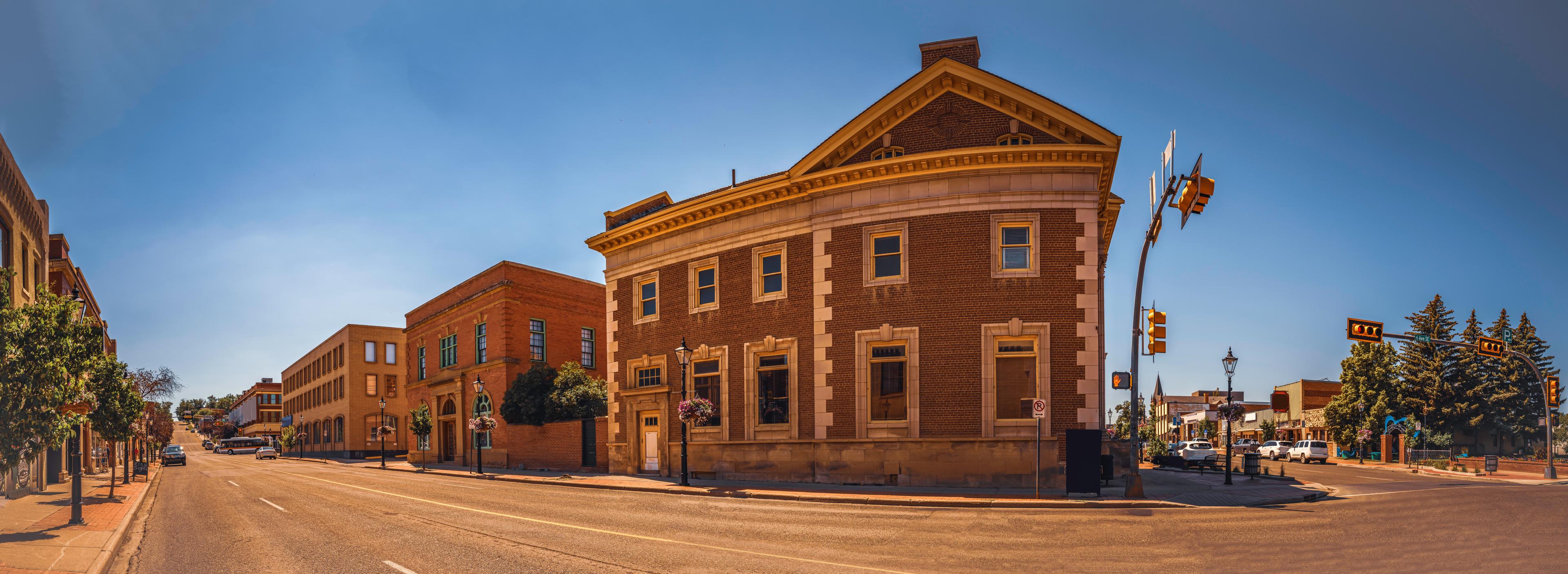 A sunny street view in downtown Medicine Hat, Alberta, showcasing historic brick buildings, tree-lined sidewalks, and a quiet intersection under a clear blue sky.