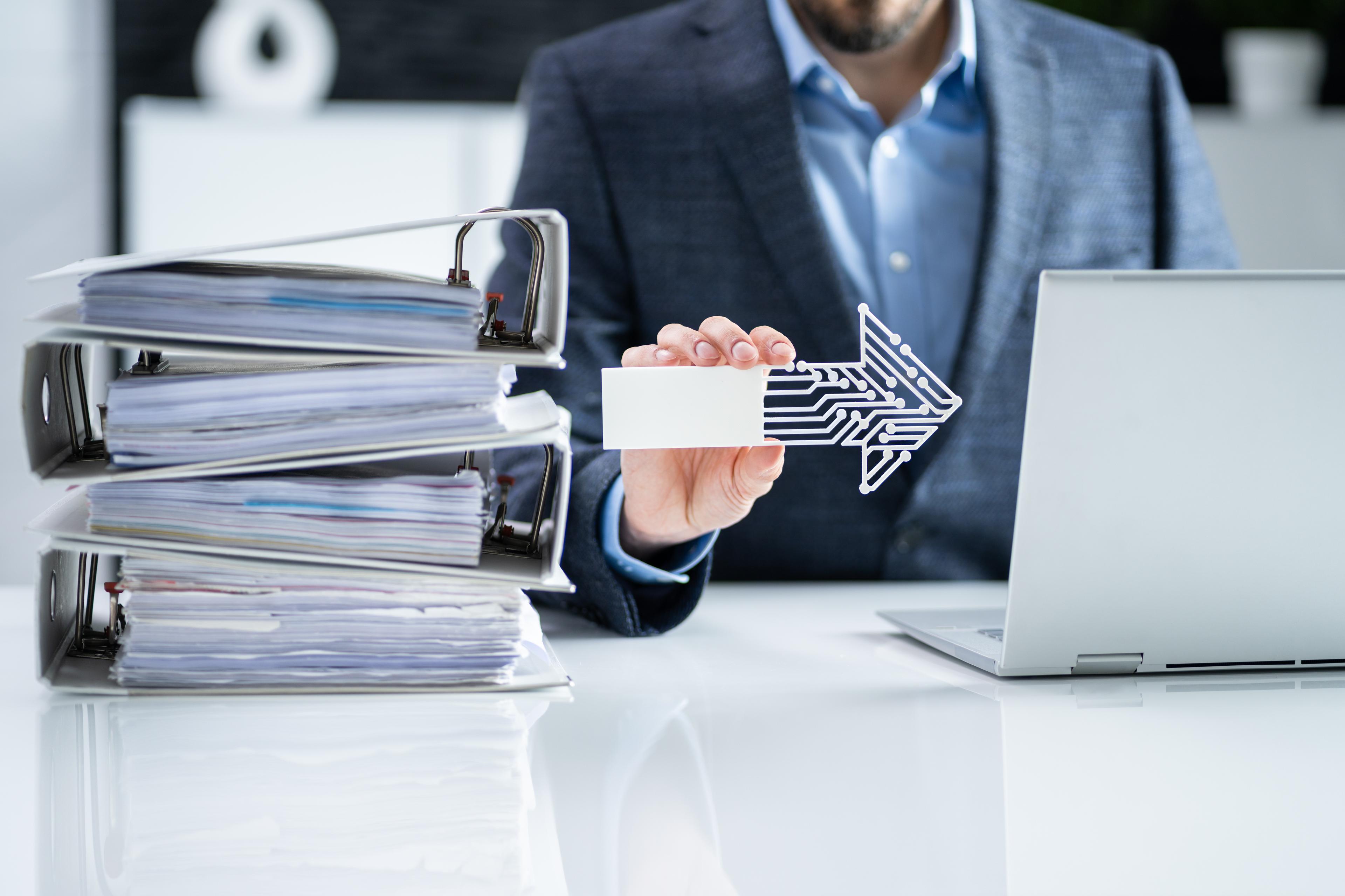 Digital records management and paperless transformation concept with businessman transitioning documents to digital system using laptop.