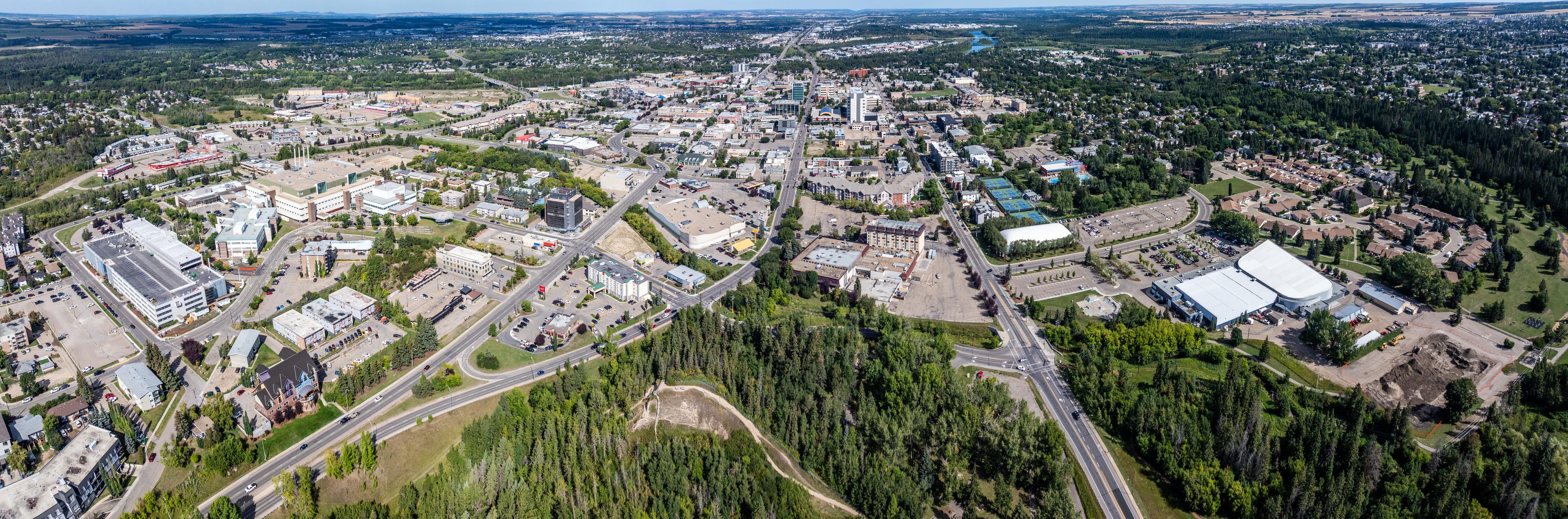 An expansive aerial view of Red Deer, Alberta, highlighting the city's downtown area, residential neighborhoods, and surrounding greenery under a clear blue sky.