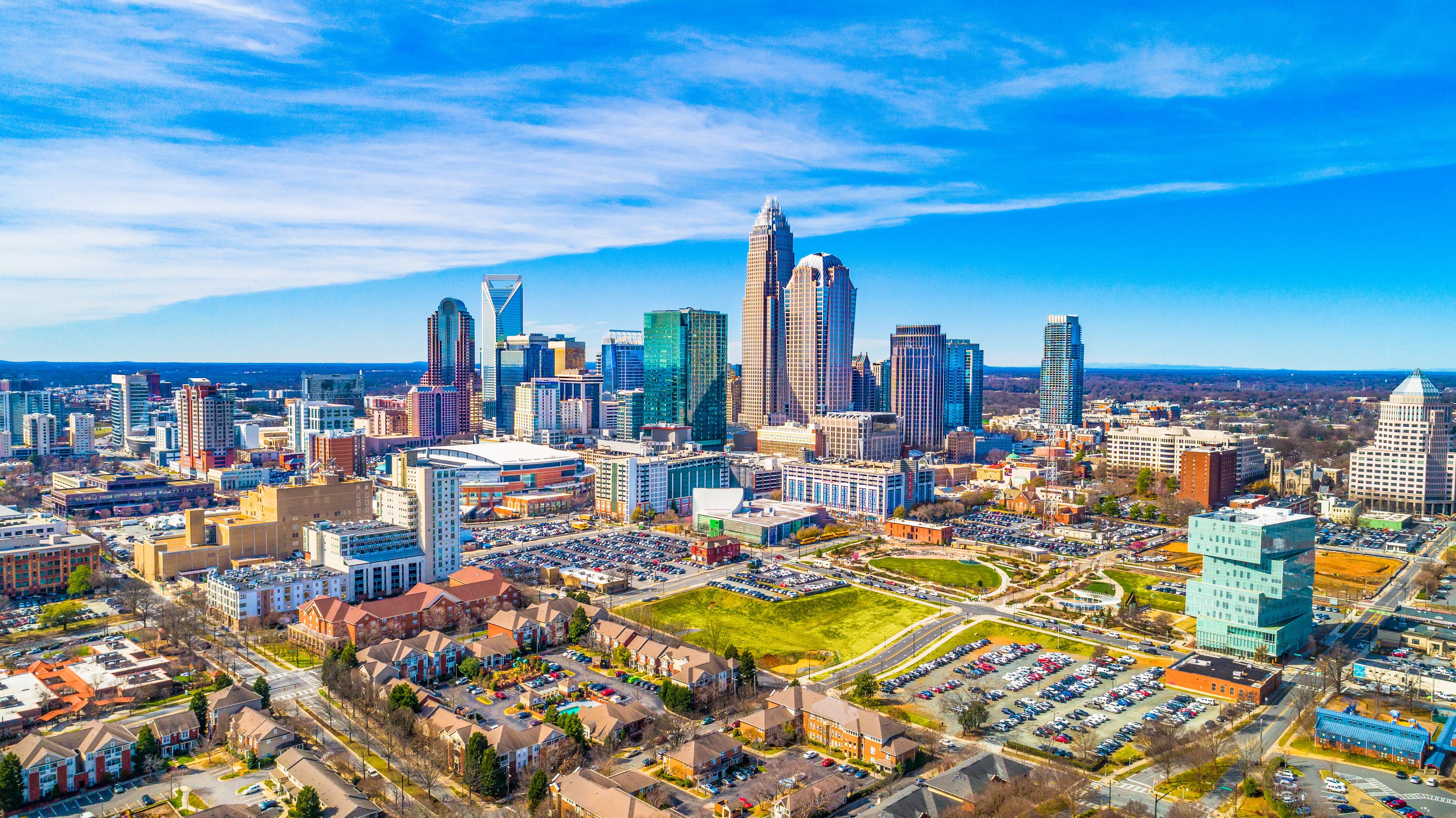Panoramic aerial view of Uptown Charlotte, North Carolina, showcasing a vibrant skyline, major landmarks, and surrounding residential neighborhoods under a clear blue sky.