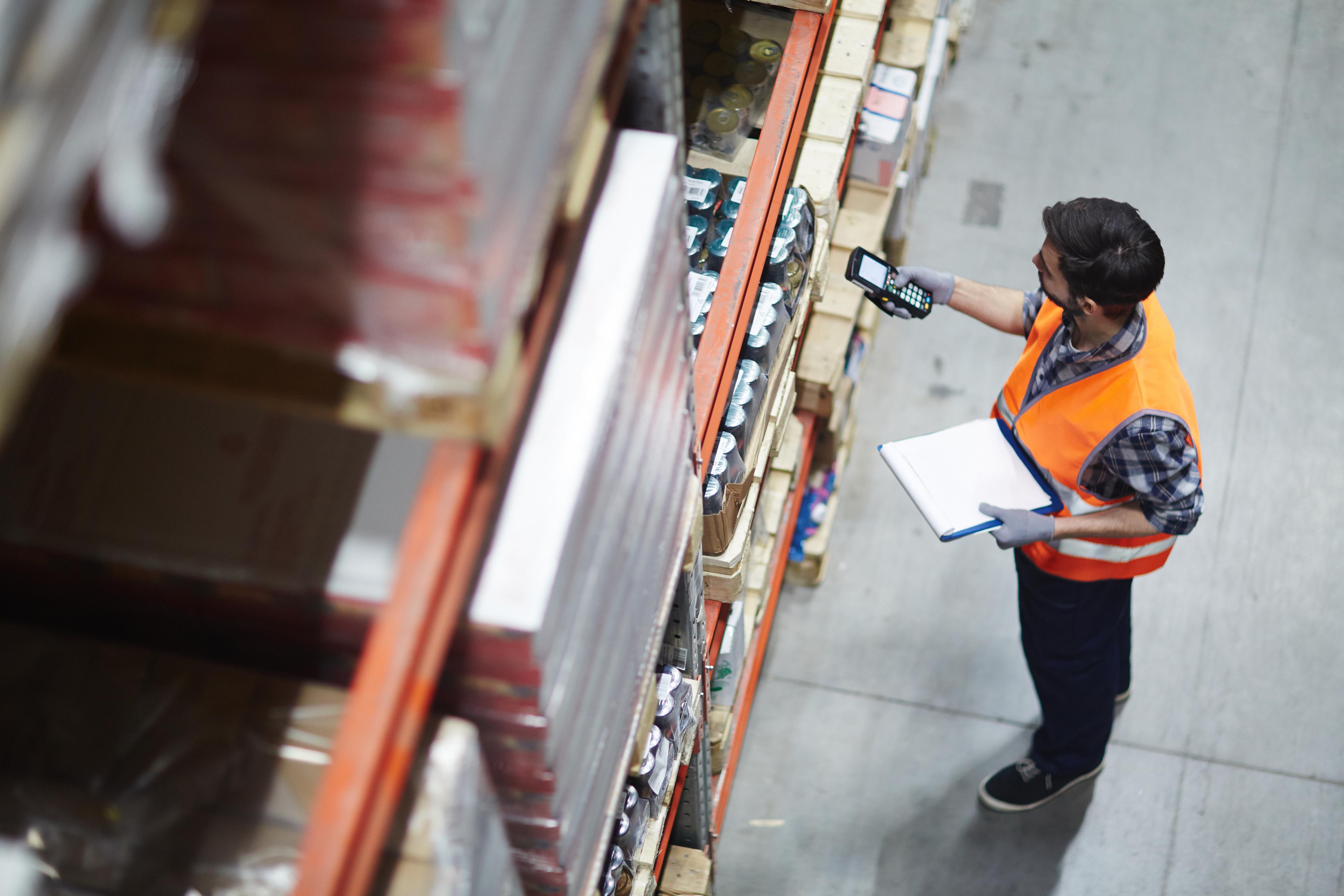 Inventory control specialist using handheld scanner for stocktaking in a warehouse storage aisle.