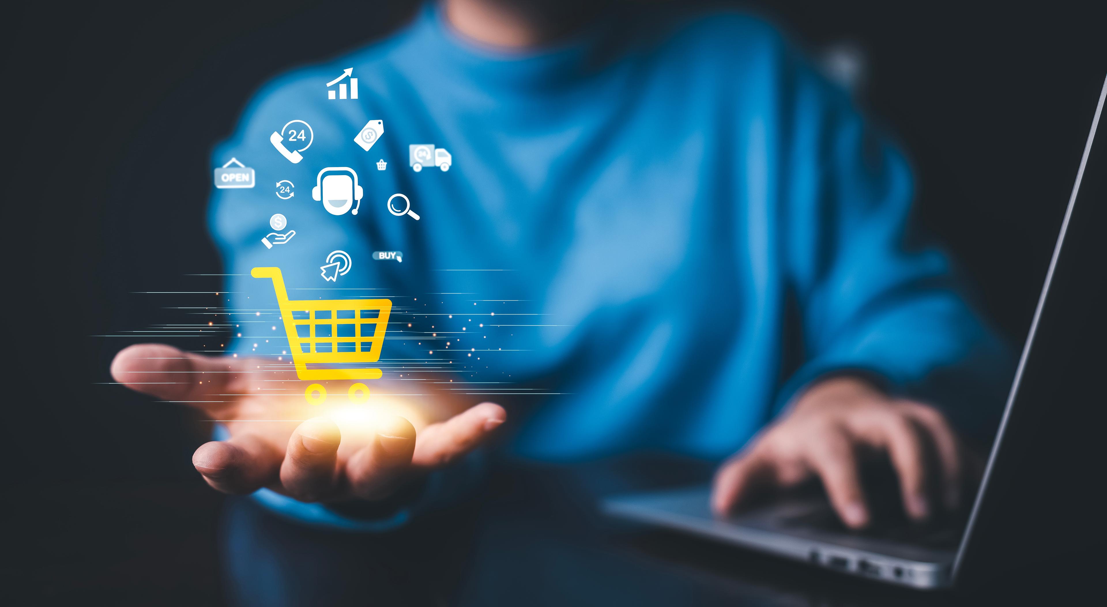 Person using a laptop with a glowing digital shopping cart icon and e-commerce symbols hovering above their hand, representing online retail and digital transactions.