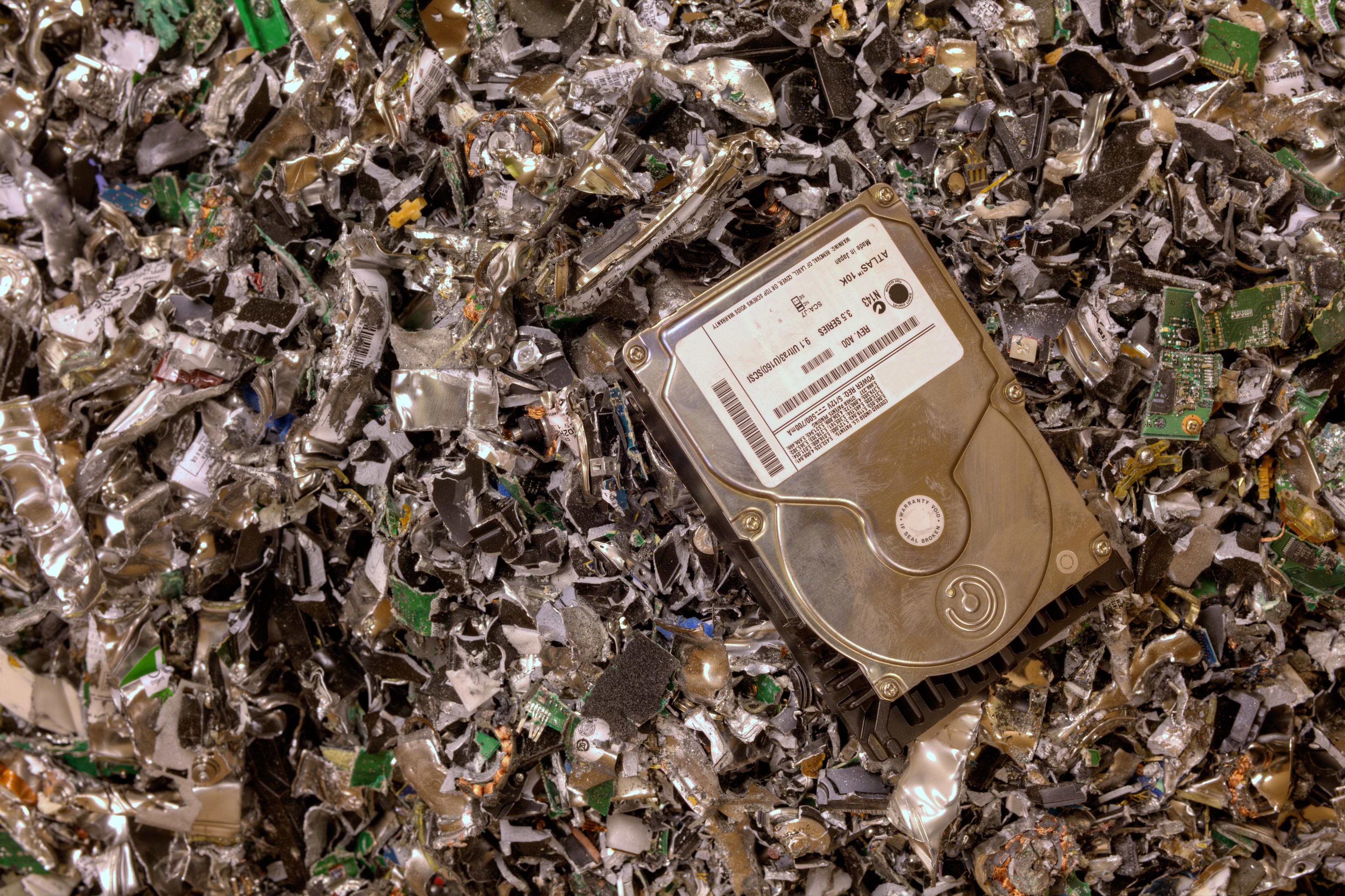 A hard drive rests on a pile of shredded electronics, representing secure destruction of data and e-waste for compliance and cybersecurity.